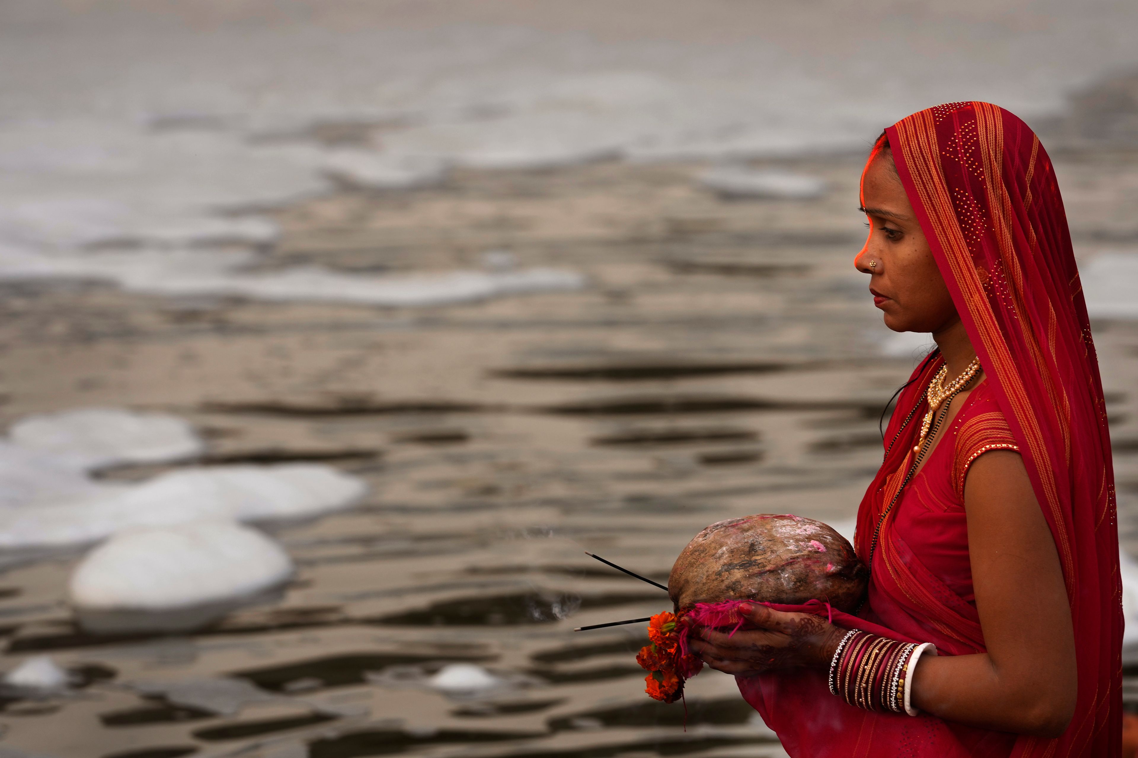 A devotee prays on the banks of the river Yamuna as toxic foam flows during Chhath festival in Noida, near New Delhi, India, Thursday, Nov. 7, 2024. (AP Photo/Manish Swarup)