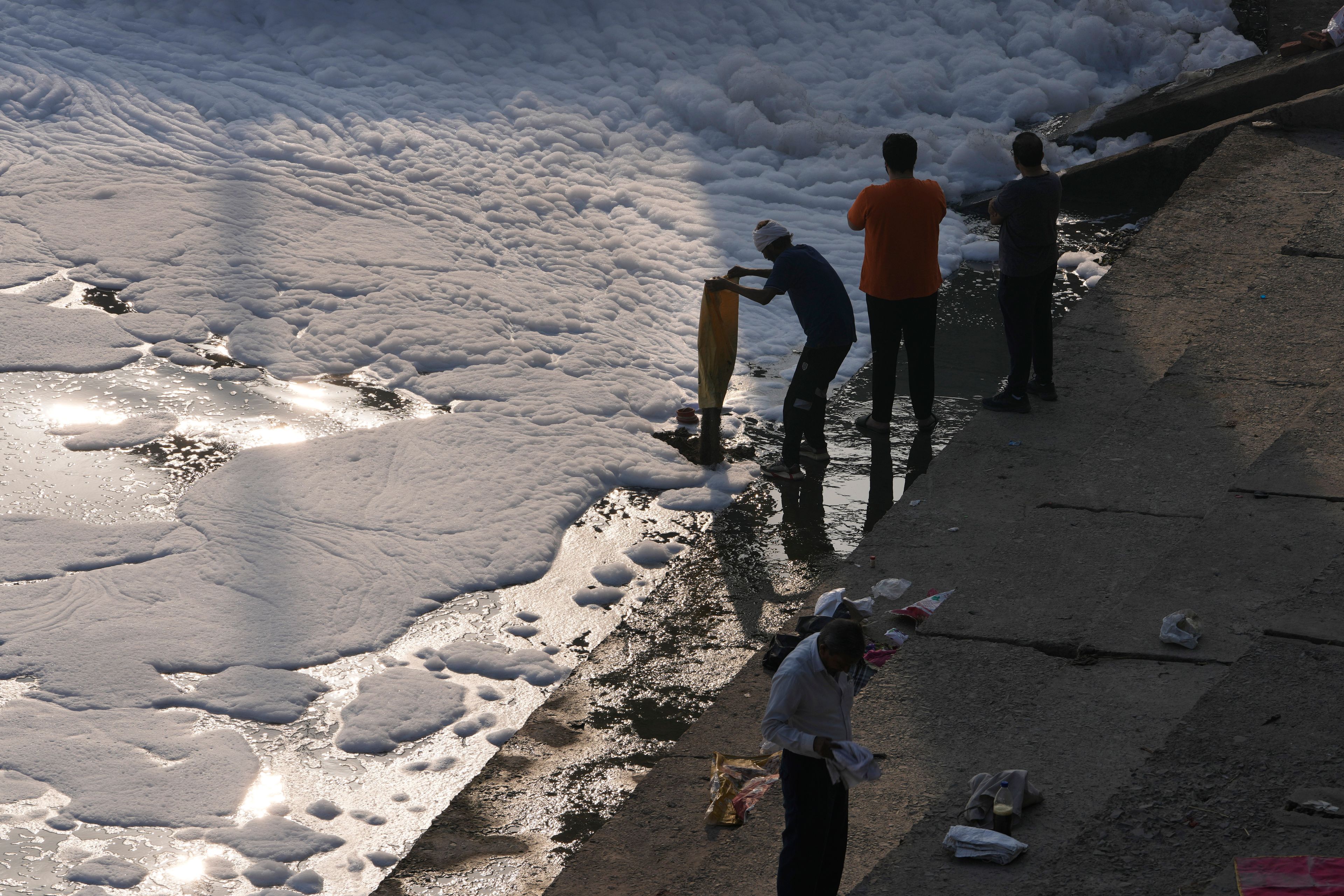 A person empties a bag of garbage in the the river Yamuna filled with toxic foams in New Delhi, India, Tuesday, Oct. 29, 2024. (AP Photo/Manish Swarup)