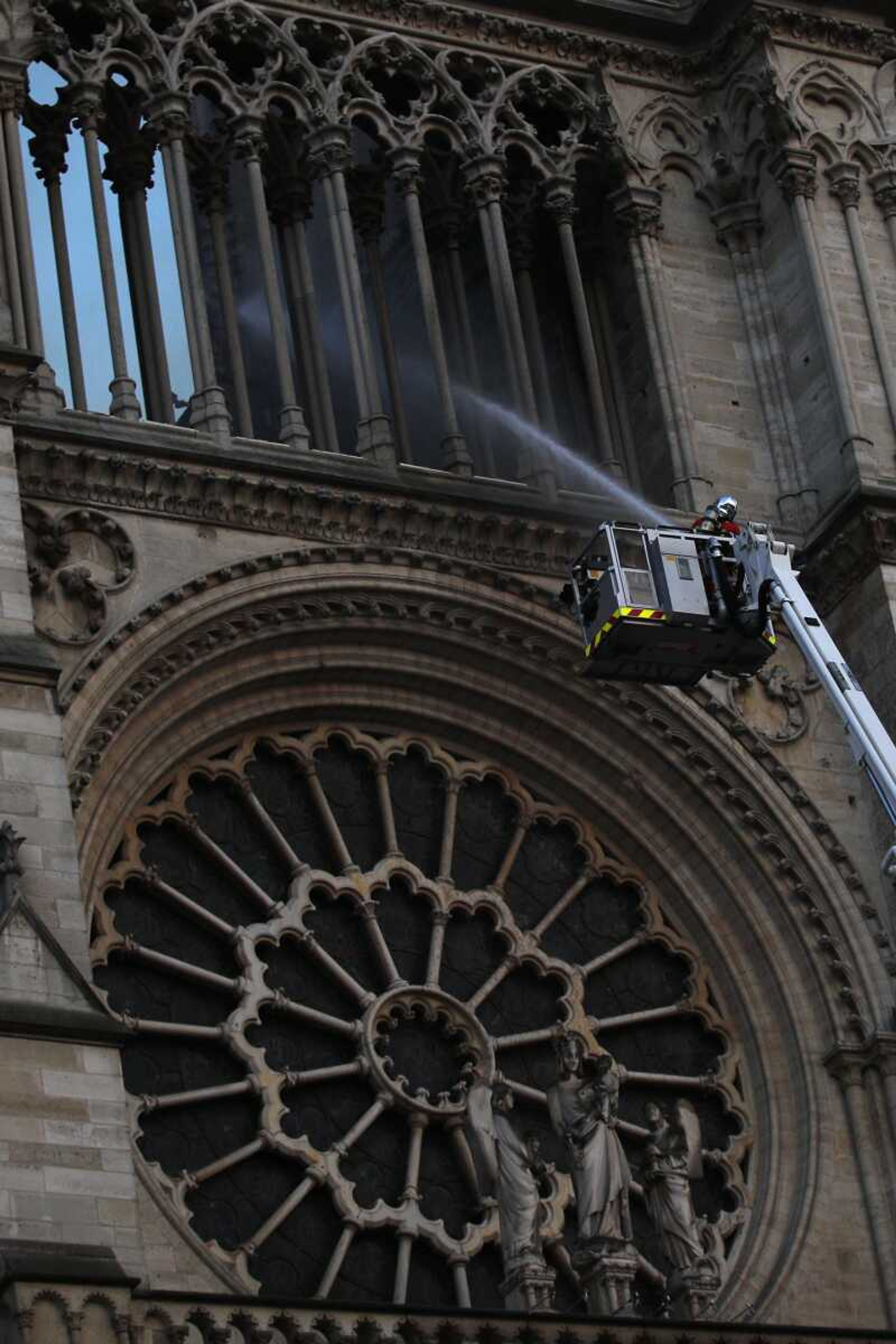 A fire fighter tackles the blaze as flames and smoke rise while Notre Dame cathedral is burning in Paris, Monday, April 15, 2019. A catastrophic fire engulfed the upper reaches of Paris' soaring Notre Dame Cathedral as it was undergoing renovations Monday, threatening one of the greatest architectural treasures of the Western world as tourists and Parisians looked on aghast from the streets below. (AP Photo/Francois Mori)