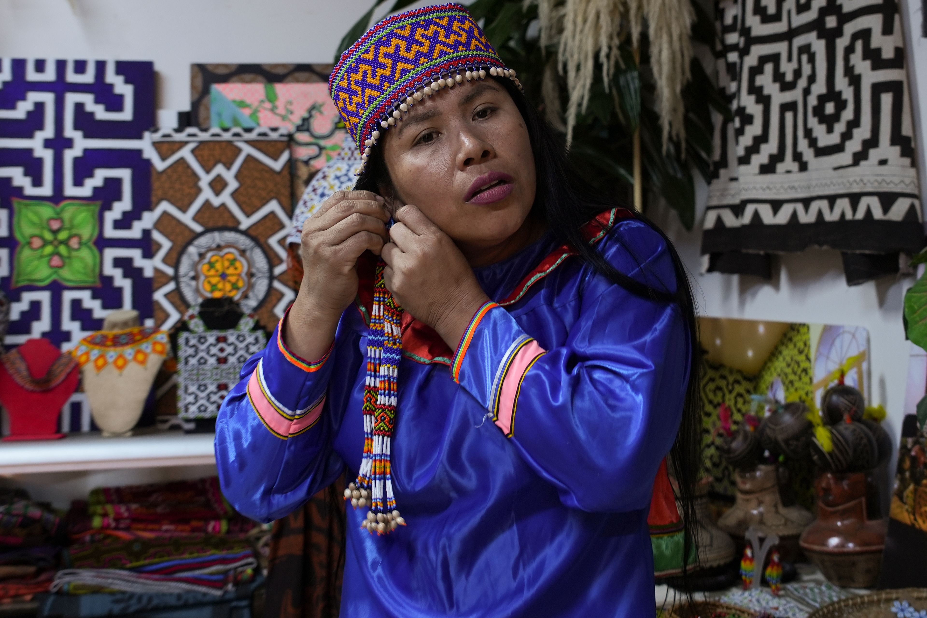 Sadith Silvano, from Paoyhan, a Shipibo-Konibo Indigenous community in the Amazon, puts on an earring at her home and workshop where she hand-paints textiles in Lima, Peru, Saturday, Oct. 19, 2024. “When we paint, we listen to the inspiration that comes from the music and connect to nature, to our elders,” said Silvano. (AP Photo/Guadalupe Pardo)