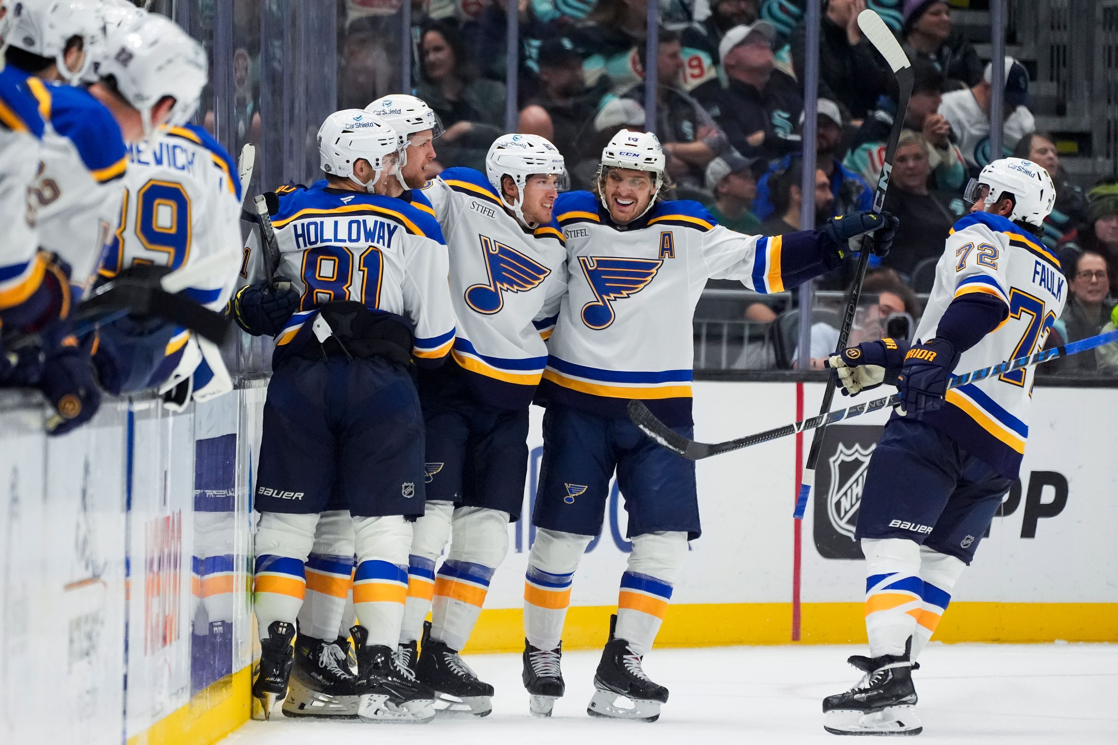 St. Louis Blues center Dylan Holloway (81) hugs defenseman Philip Broberg to celebrate Broberg's goal as defenseman Justin Faulk (72) and center Robert Thomas, second from left, join them to celebrate during the second period of an NHL hockey game against the Seattle Kraken, Tuesday, Oct. 8, 2024, in Seattle. (AP Photo/Lindsey Wasson)