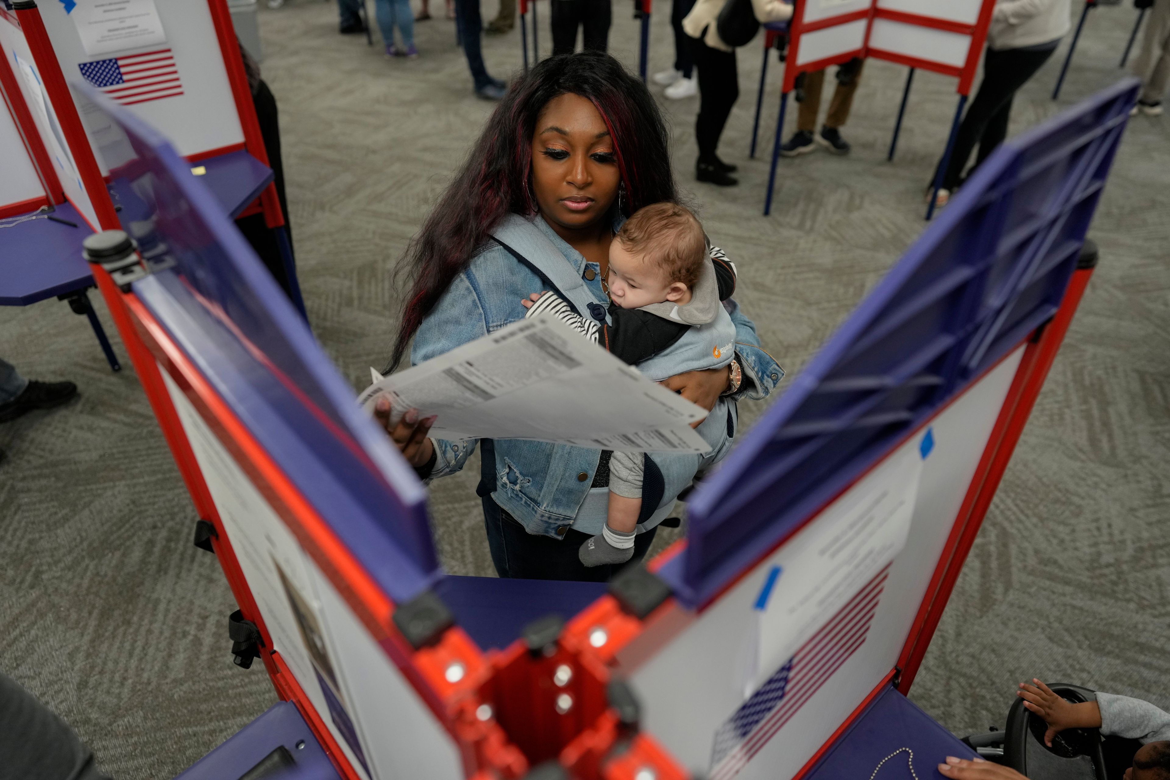 First-time voter Kayria Hildebran holds baby Kayden Hildebran as she fills out her ballot during in-person early voting at Hamilton County Board of Elections, Thursday, Oct. 31, 2024, in Cincinnati. (AP Photo/Carolyn Kaster)