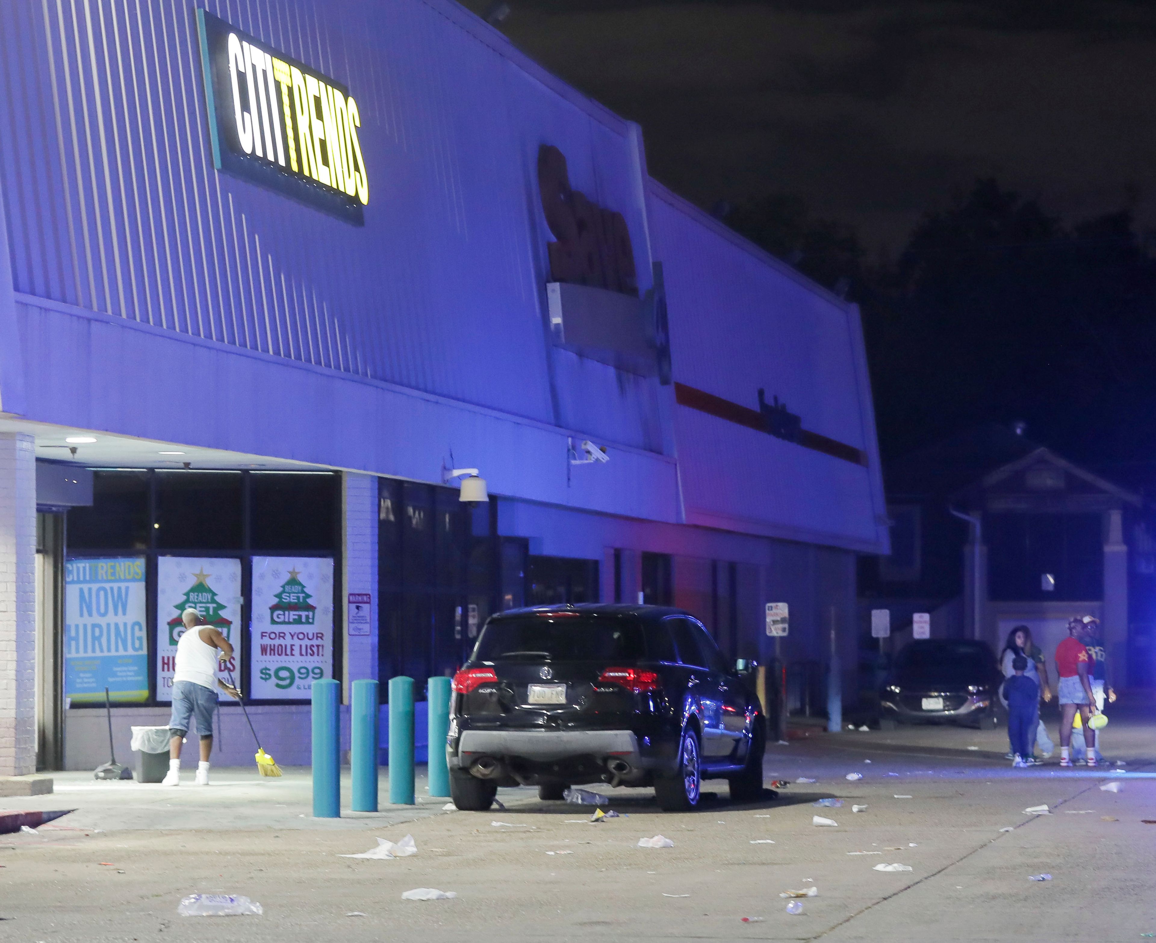 An employee with Cititrends sweeps the ground at a Save O Lot parking lot where several people were shot and killed in New Orleans, Sunday Nov. 17, 2024. (David Grunfeld/The Times-Picayune/The New Orleans Advocate via AP)