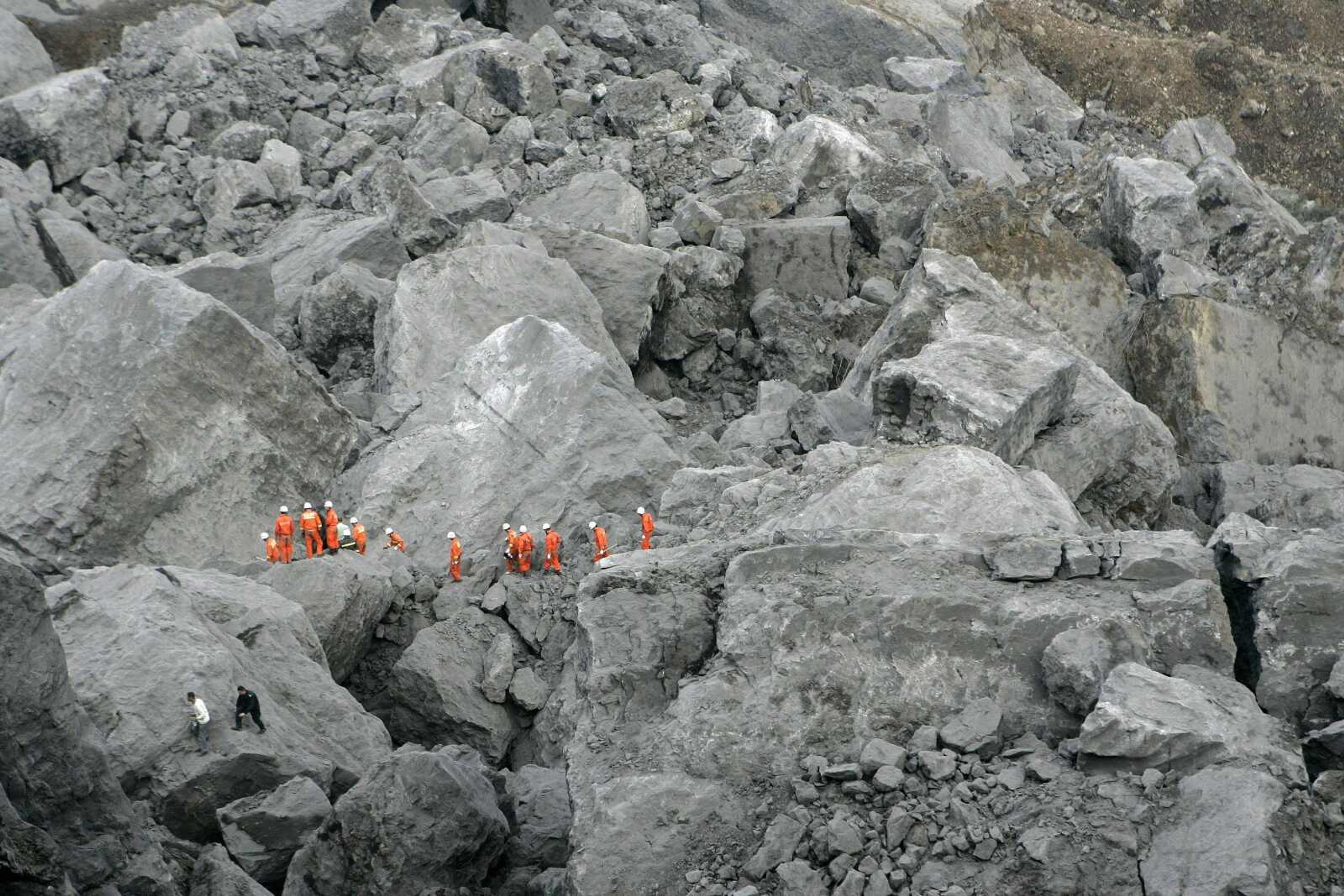 Rescue personnel walks past huge rocks as they search for survivors at the site where a landslide occurred Friday in Wulong county in southwest China's Chongqing Municipality, Saturday June 6, 2009. A landslide buried an iron ore plant and several homes, killing at least 26 people and leaving dozens missing in a valley in southwestern China, state television said Saturday. (AP Photo) ** CHINA OUT **