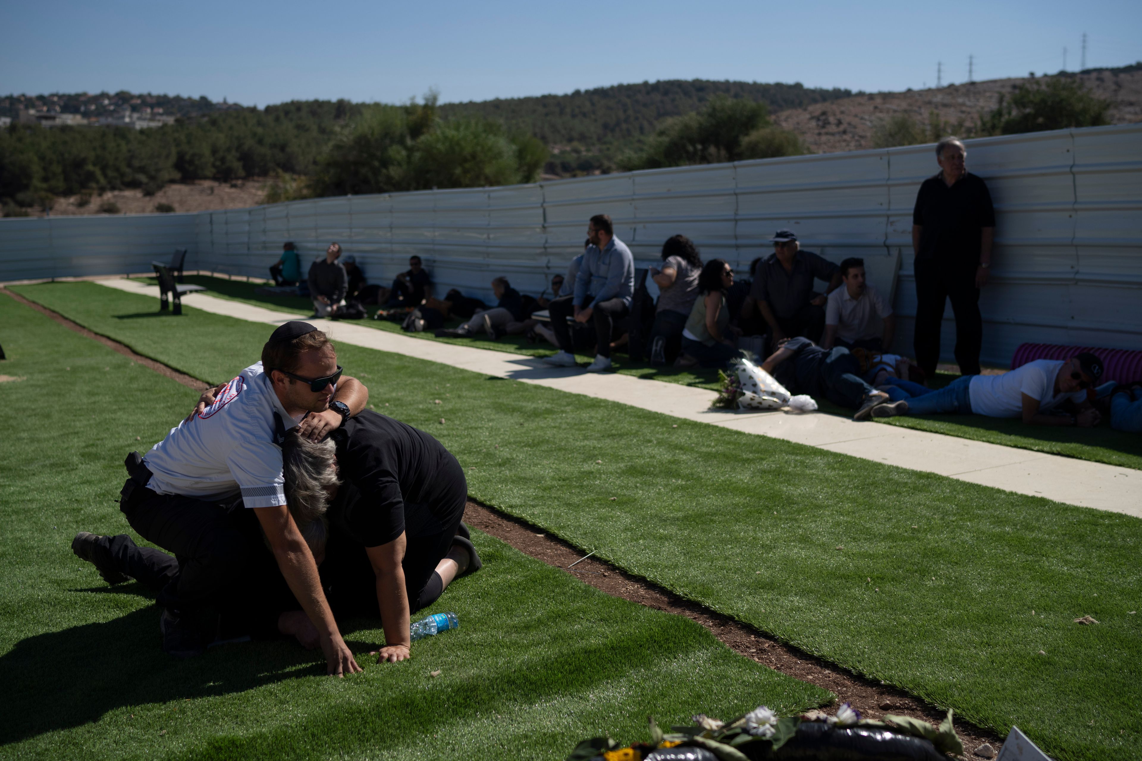 People take cover as a siren warns of incoming rockets during the funeral of Alexei Popov, who was killed during a rocket attack fired from Lebanon last weekend, at the Tel Regev cemetery in the outskirts of Haifa, northern Israel, Monday, Oct. 21, 2024. (AP Photo/Leo Correa)