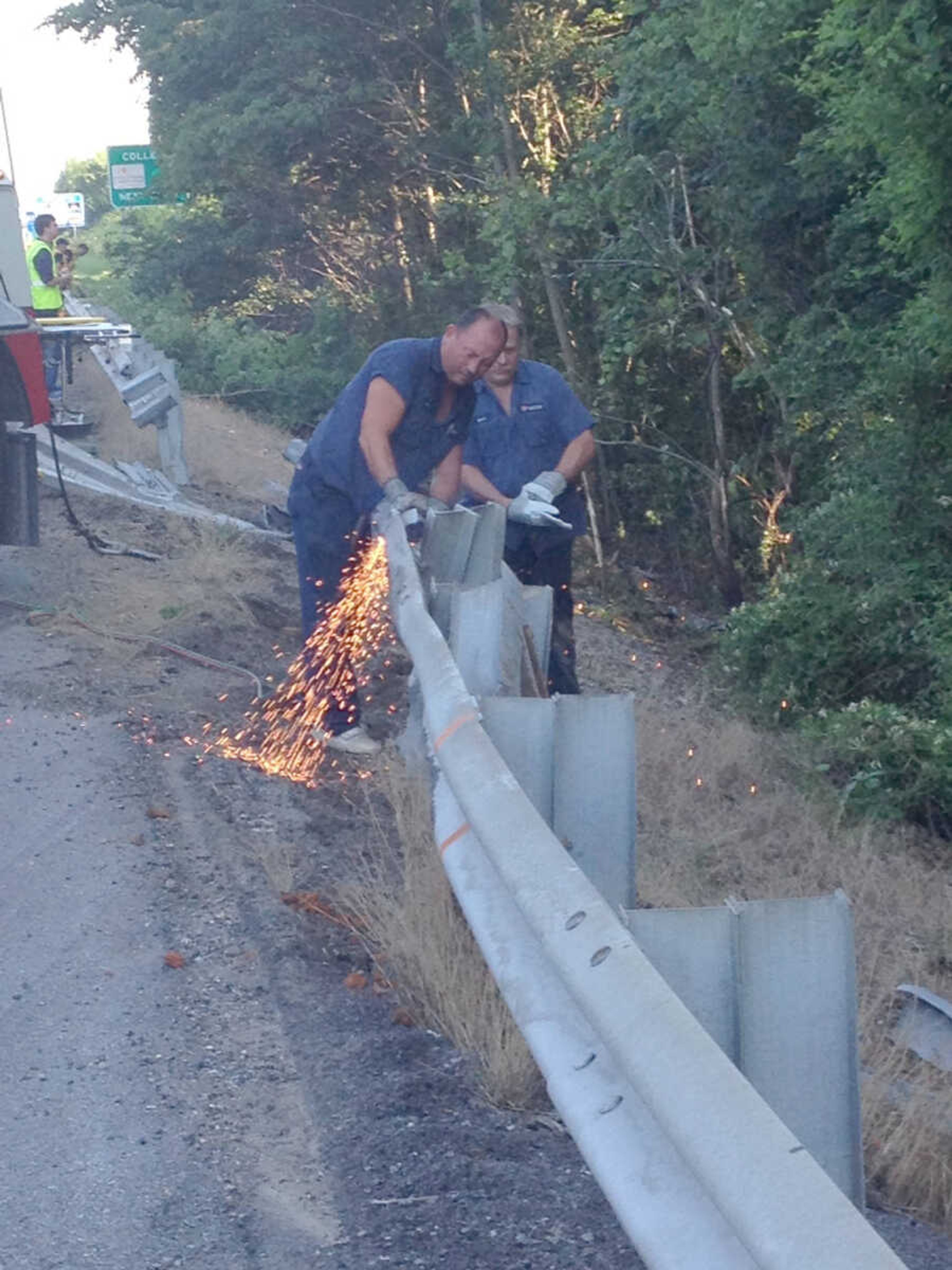 Men use torches to cut a section of guardrail on southbound Interstate 55 near the 97 mile marker Wednesday in preparation for towing a tractor-trailer up an embankment. The tractor-trailer crashed through the rail, and the driver was killed. (Emily Priddy)