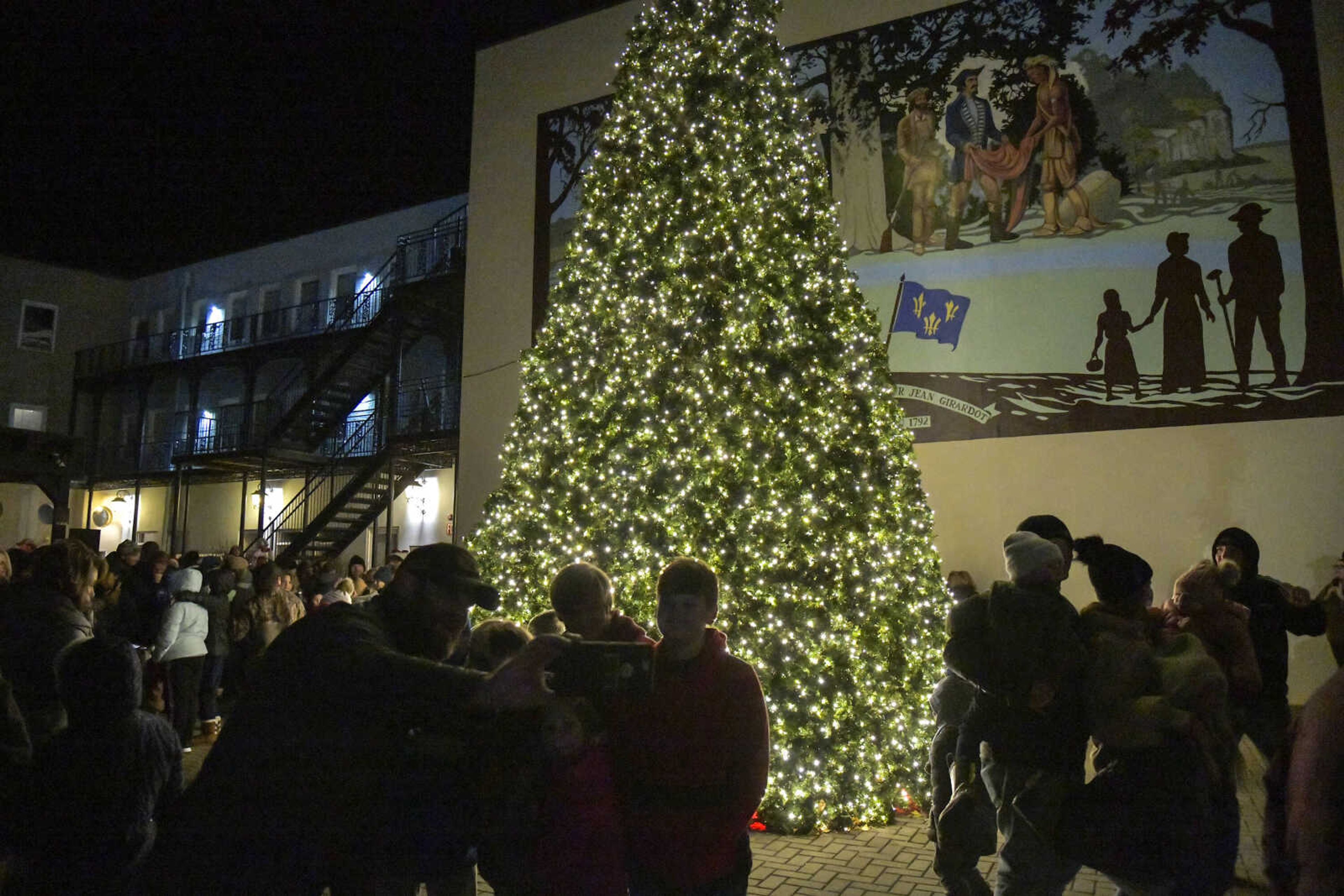 Attendees take pictures near the lit tree during the 3rd Annual Old Town Cape Christmas Tree Lighting on Friday in Cape Girardeau.