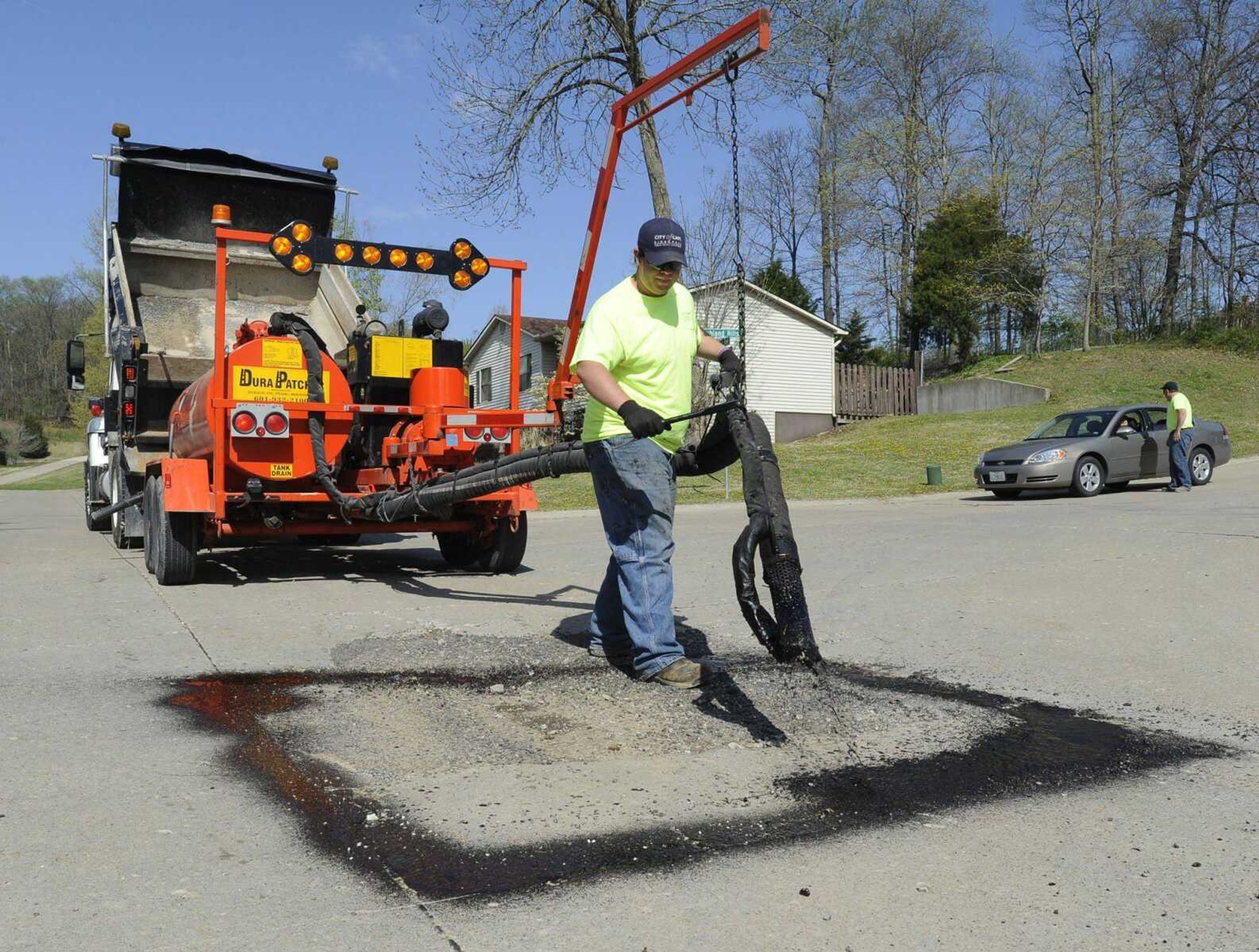 Jason Beasley operates the DuraPatcher machine on a large pothole Friday in Cape Girardeau. The machine spreads oil heated to 160 degrees. Then it covers the area with rock for a longer-term solution than using cold mix for pothole repairs. (Fred Lynch)