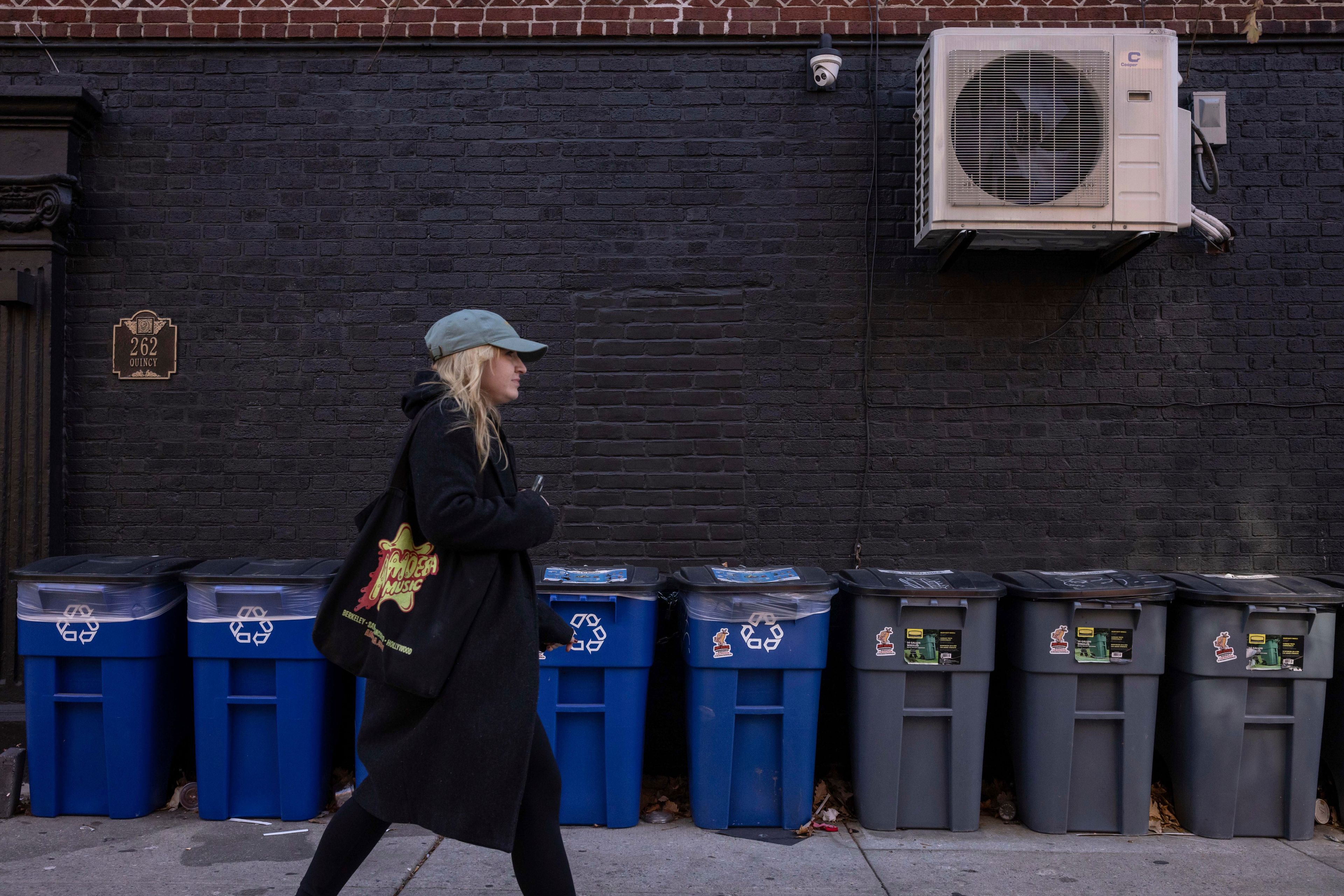 A person walks in front of trash bins, Friday, Nov. 15, 2024, in the Brooklyn borough of New York. (AP Photo/Yuki Iwamura)