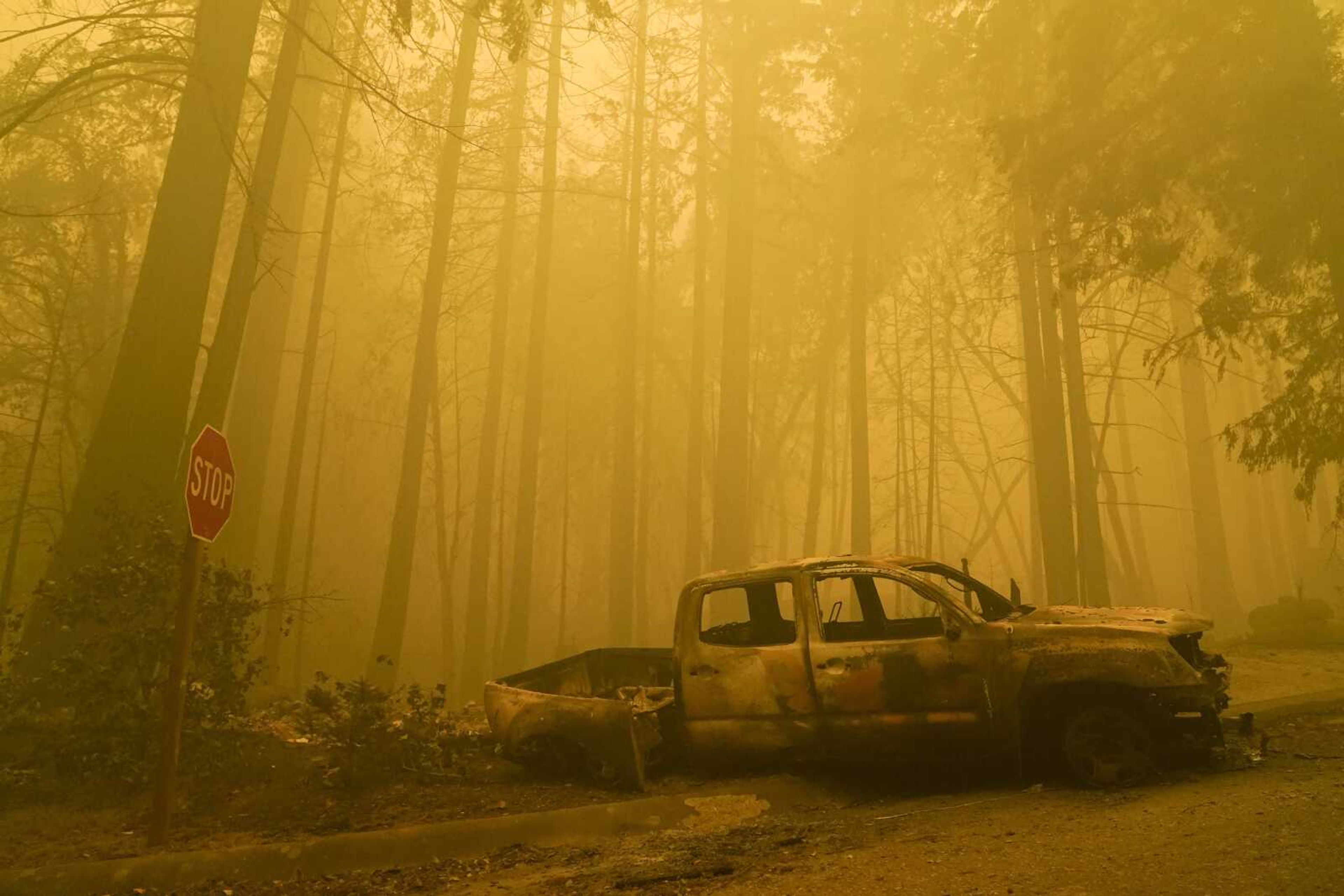 A burned out vehicle is left in front of a fire-ravaged residence as smoke from the CZU August Lightning Complex Fire fills the sky Saturday in Boulder Creek, California.