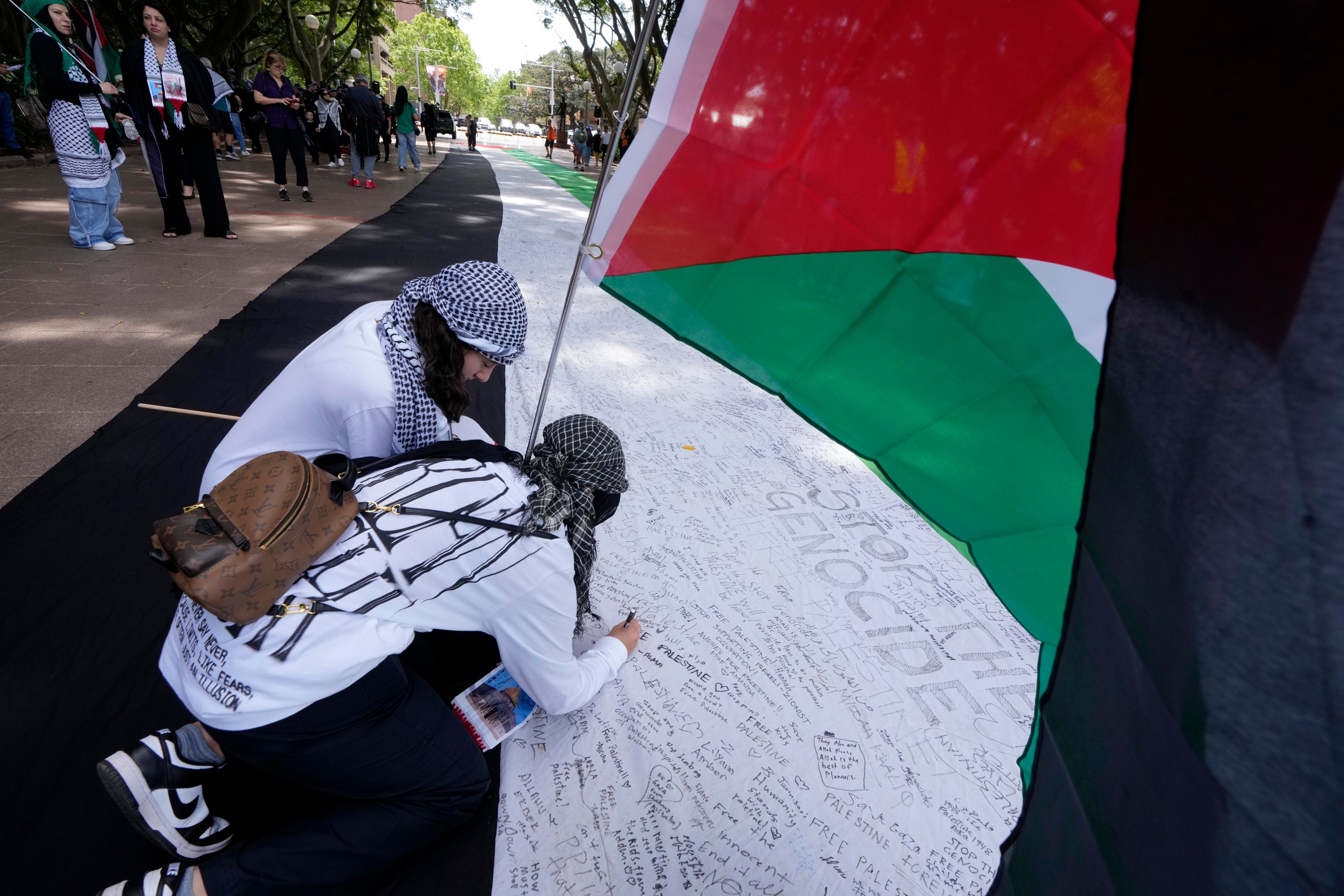 Two young women write on a giant flag as pro-Palestinian supporters rally in Sydney, Sunday, Oct. 6, 2024. (AP Photo/Rick Rycroft)