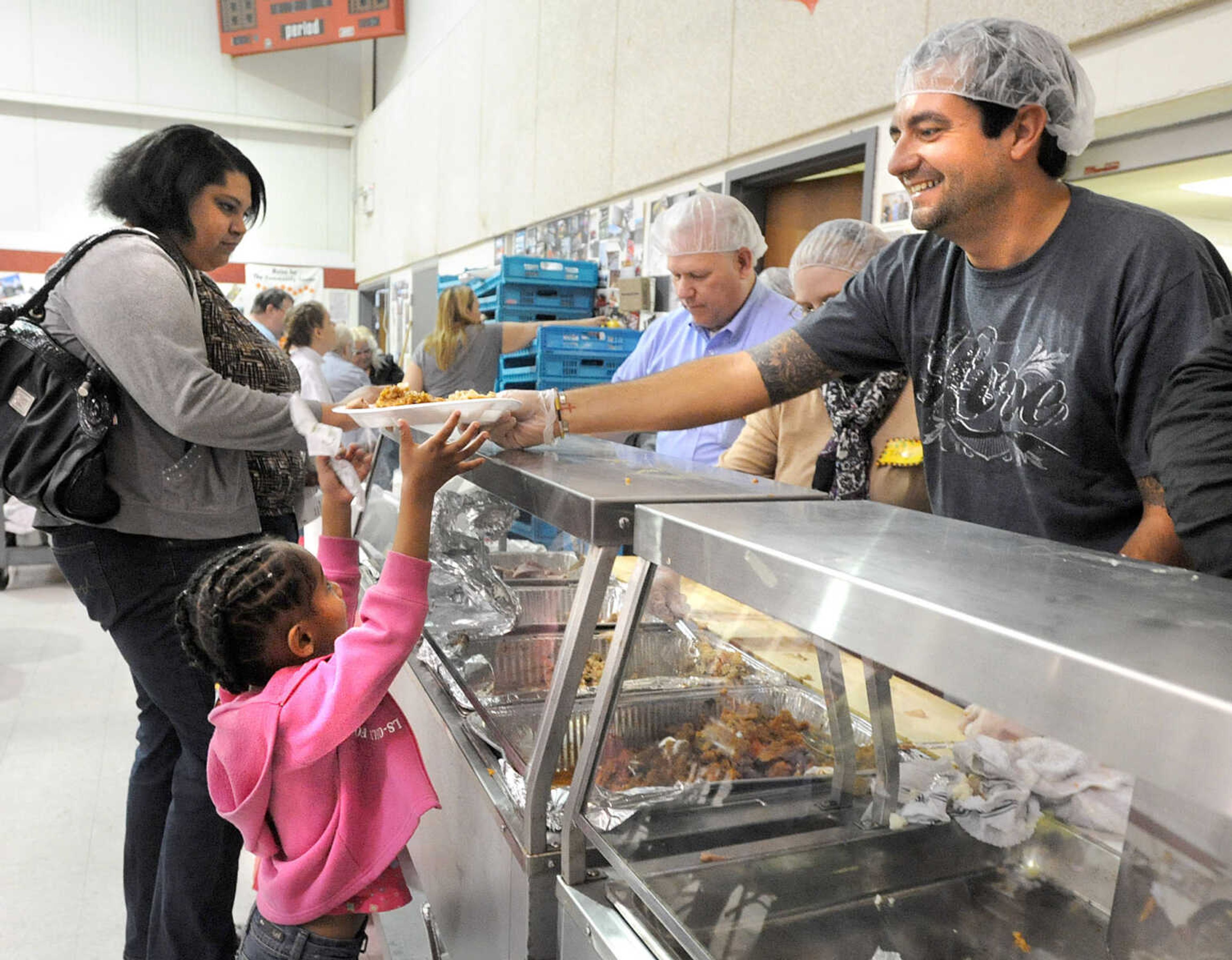 LAURA SIMON ~ lsimon@semissourian.com
Lanisha Zahlen, 5, stands on her tiptoes to reach her Thanksgiving day lunch plate from Cory Anderson at the Salvation Army in Cape Girardeau. Around 150 volunteers pitched in during the annual holiday lunch which has been serving people since 1983.