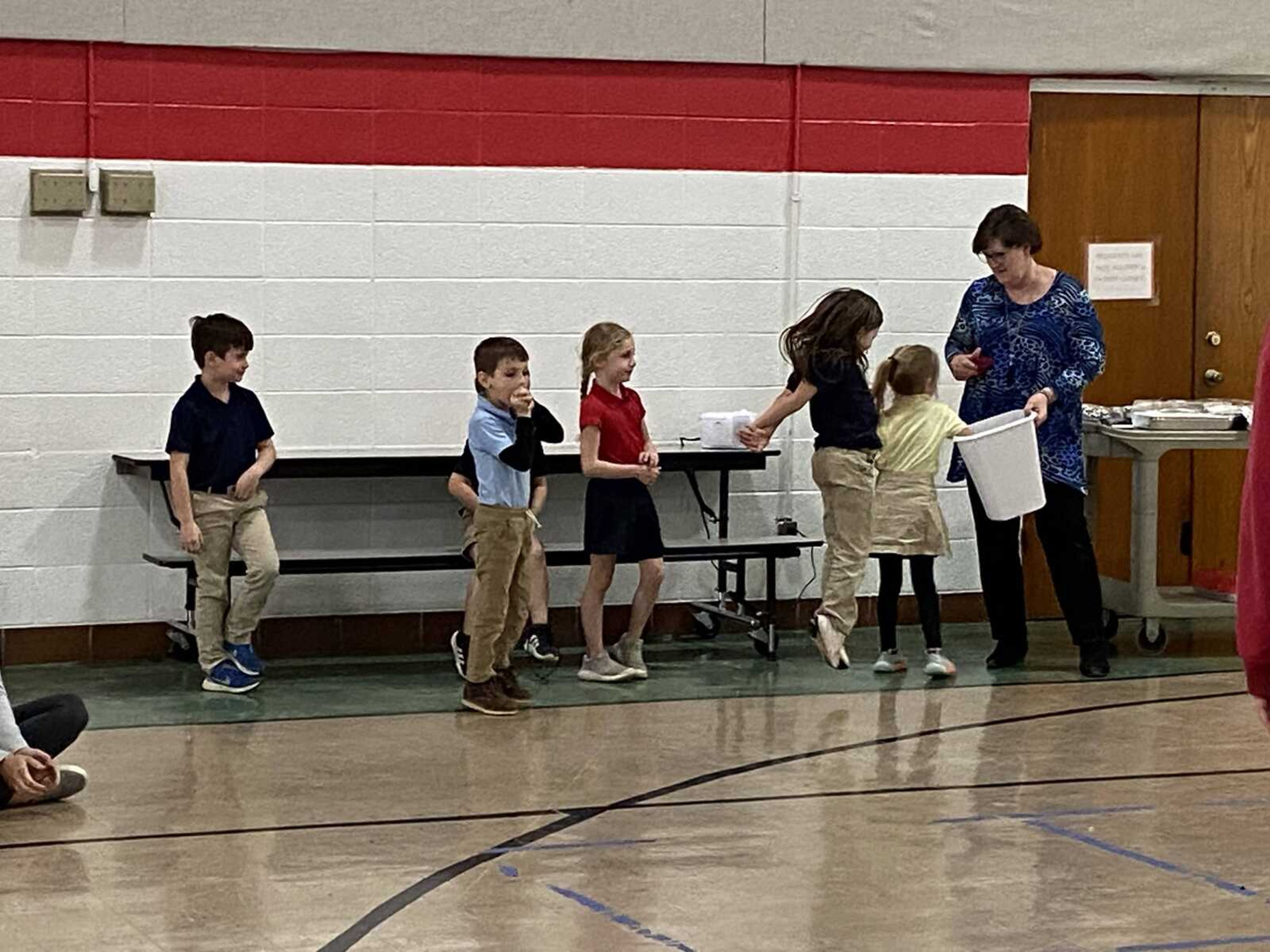 The Kindergarten students take turns pulling out a letter from the basket held by Mrs. Seyer, to find out who won a cake.