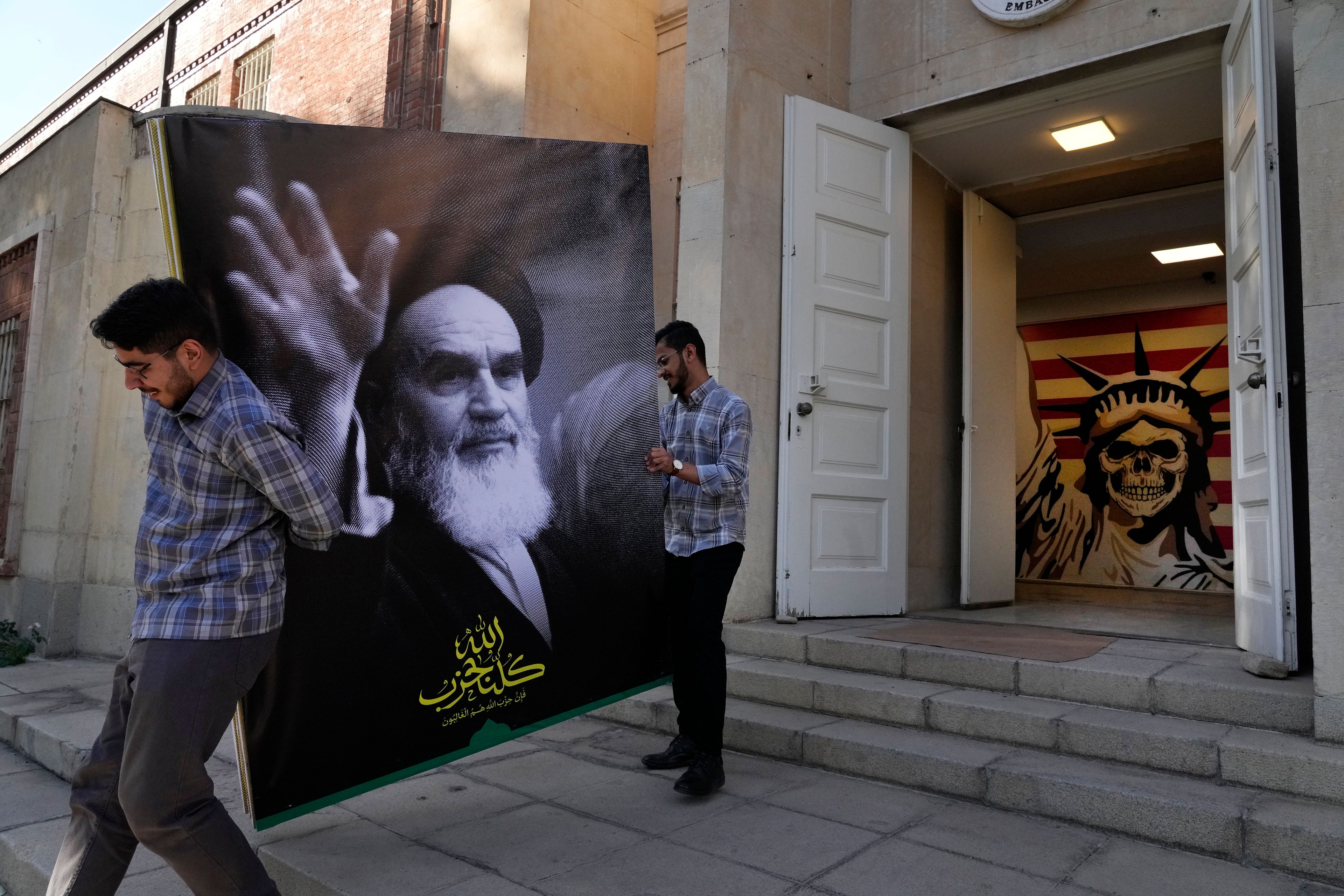 Two men carry a banner of the late Iranian revolutionary founder Ayatollah Khomeini at the entrance of the former U.S. Embassy, which has been turned into an anti-American museum, in Tehran, Iran, Tuesday, Oct. 22, 2024. (AP Photo/Vahid Salemi)