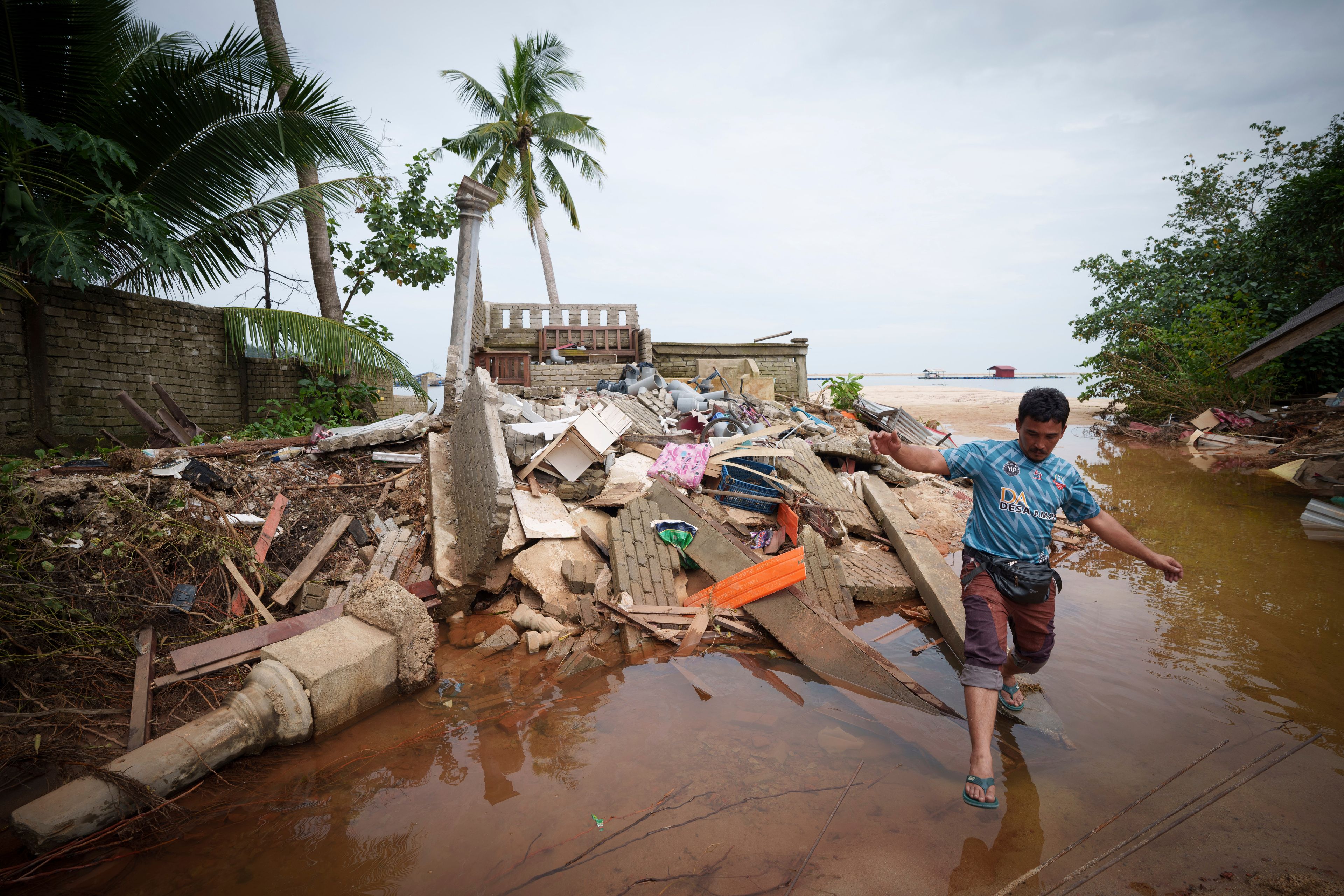 People wade through the water past a house damaged by flood in Tumpat, outskirts of Kota Bahru, Malaysia, Tuesday, Dec. 3, 2024. (AP Photo/Vincent Thian)