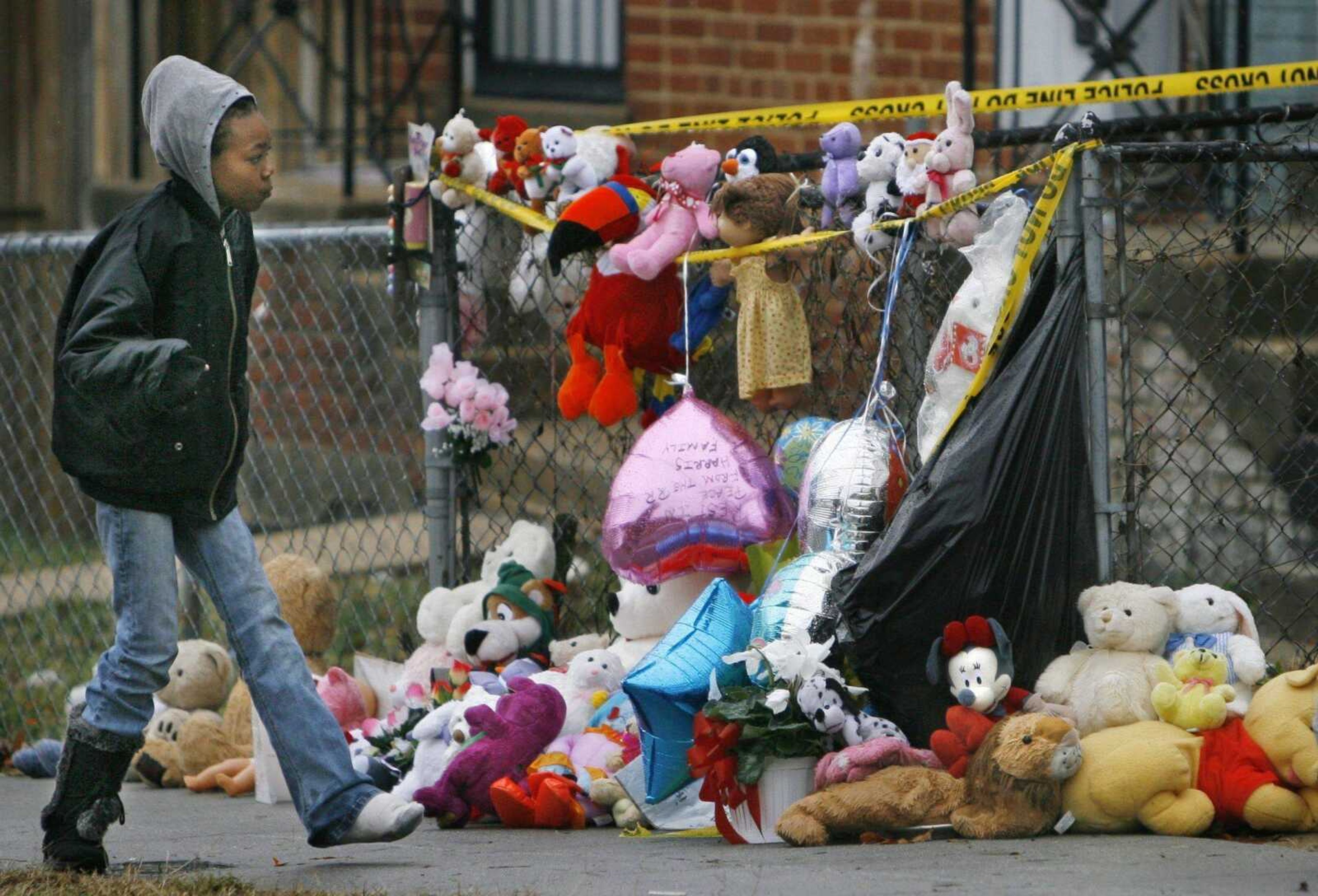 Melody Marshall, 10, of Washington, D.C., walked by a memorial of teddy bears, flowers and balloons lining the fence Friday outside the home of Banita Jacks in Washington, D.C. (Jacquelyn Martin ~ Associated Press)