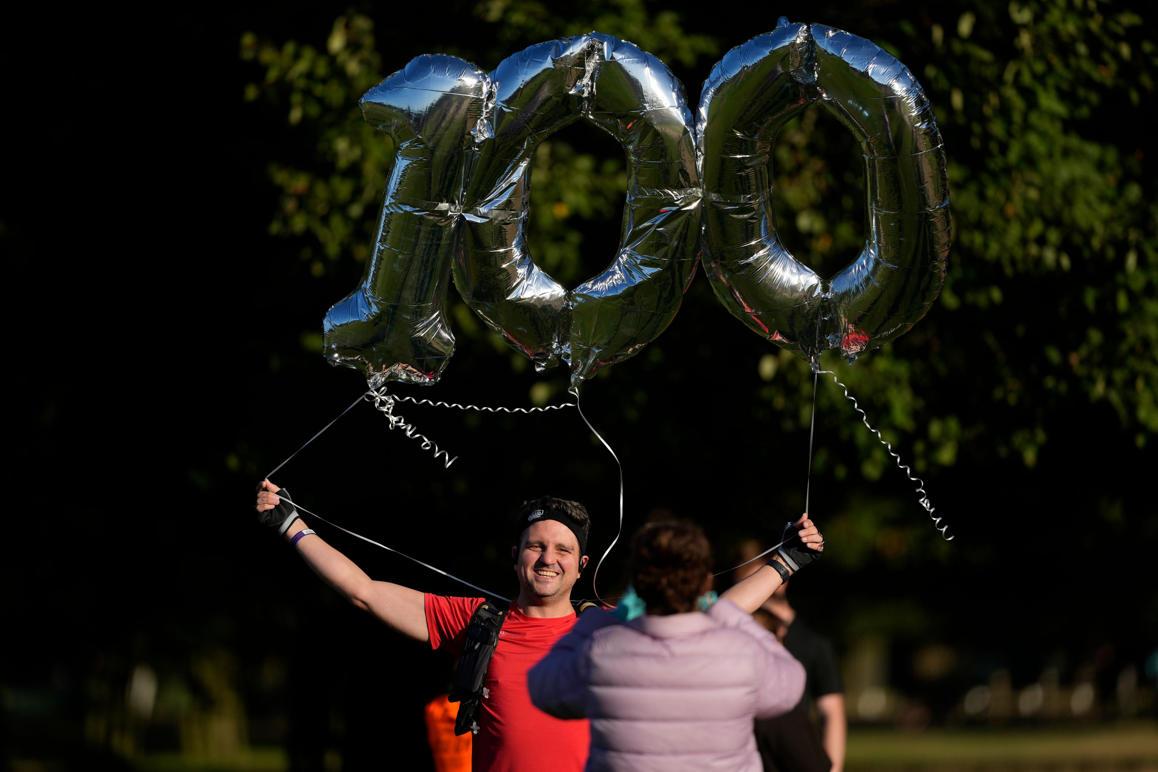 Paul Hoover holds balloons as he poses for a photo before taking part in his 100th parkrun event in Bushy Park, southwest London, Saturday, Sept. 28, 2024. (AP Photo/Alastair Grant)