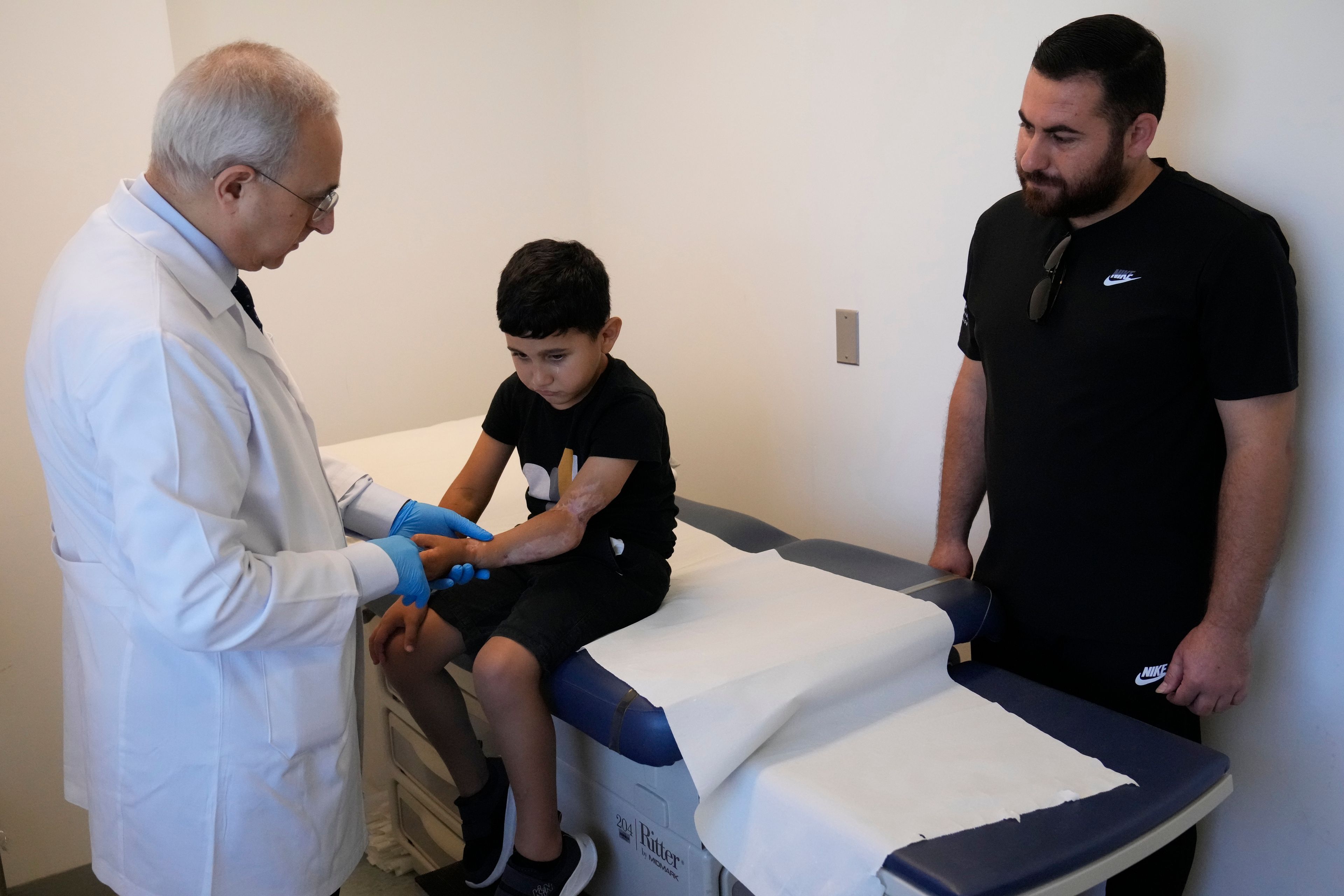 Orthopedic and spine surgeon Dr. Rachid Haidar, left, checks the arm of a Palestinian boy, Adam Afana, 5, who was brought to Lebanon from Gaza for treatment after nearly losing his left arm in an Israeli airstrike that killed his father and sister, at the American University of Beirut Medical Center, in Beirut, Lebanon, Monday, July 15, 2024. (AP Photo/Hussein Malla)