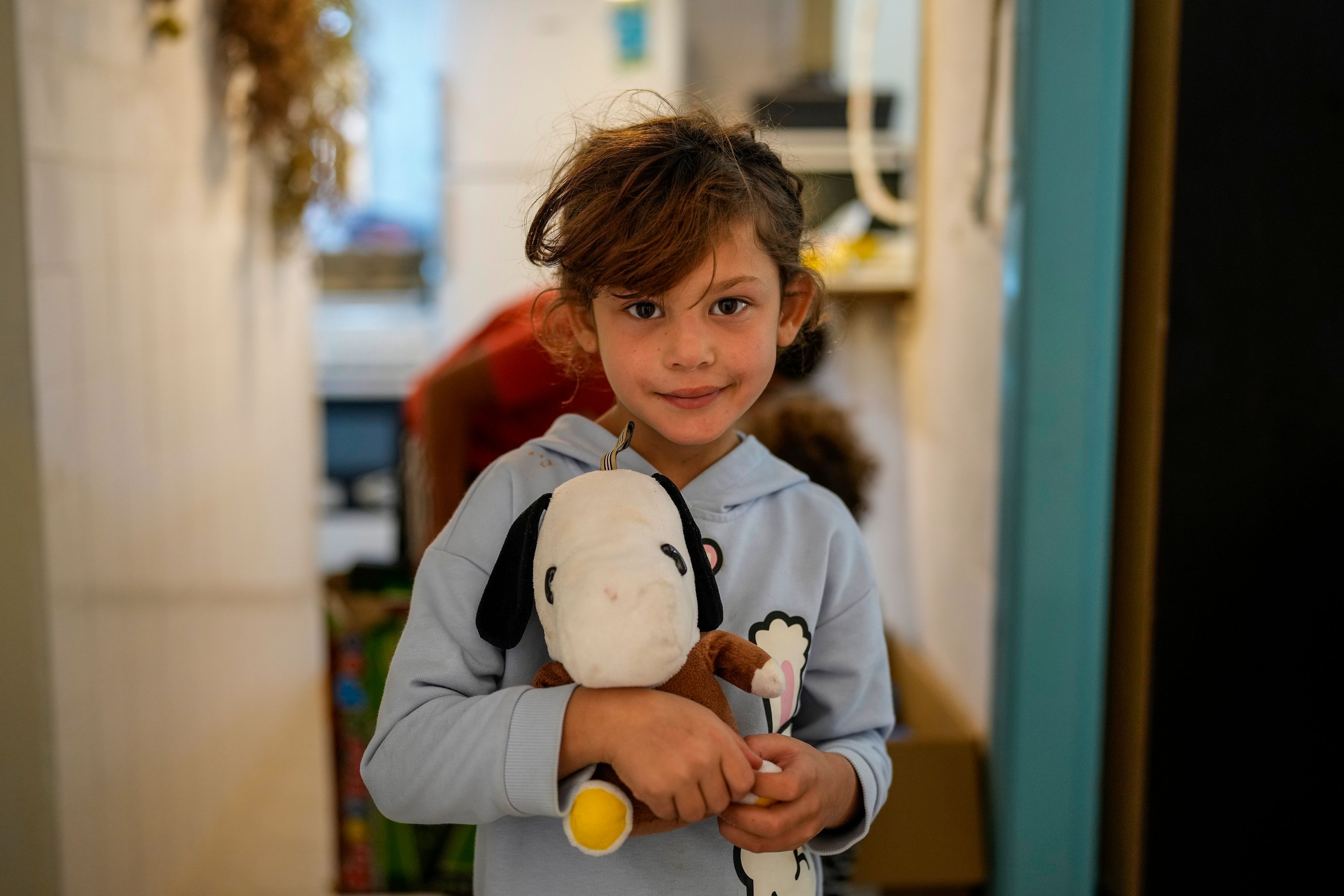 A displaced girl who fled southern Lebanon during the ongoing Hezbollah-Israel war poses for a photograph with her toy at a women's art center that has turned into a kitchen for displaced people, in the town of Aqaibe, northern Lebanon, Thursday, Oct. 24, 2024. (AP Photo/Hassan Ammar)