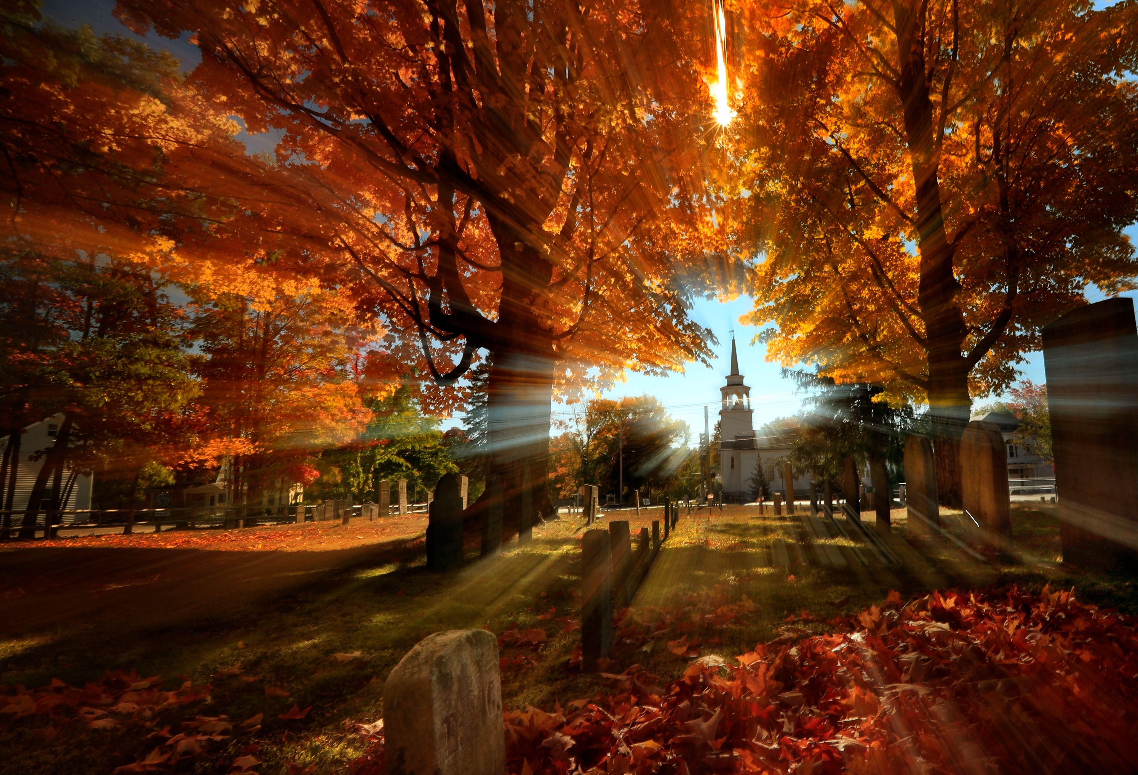 FILE - In this photo taken with a slow shutter speed, autumn's colors peak on hardwood trees in a cemetery near the Congregational Church, Monday, Oct. 10, 2016, in Cumberland, Maine. (AP Photo/Robert F. Bukaty, File)