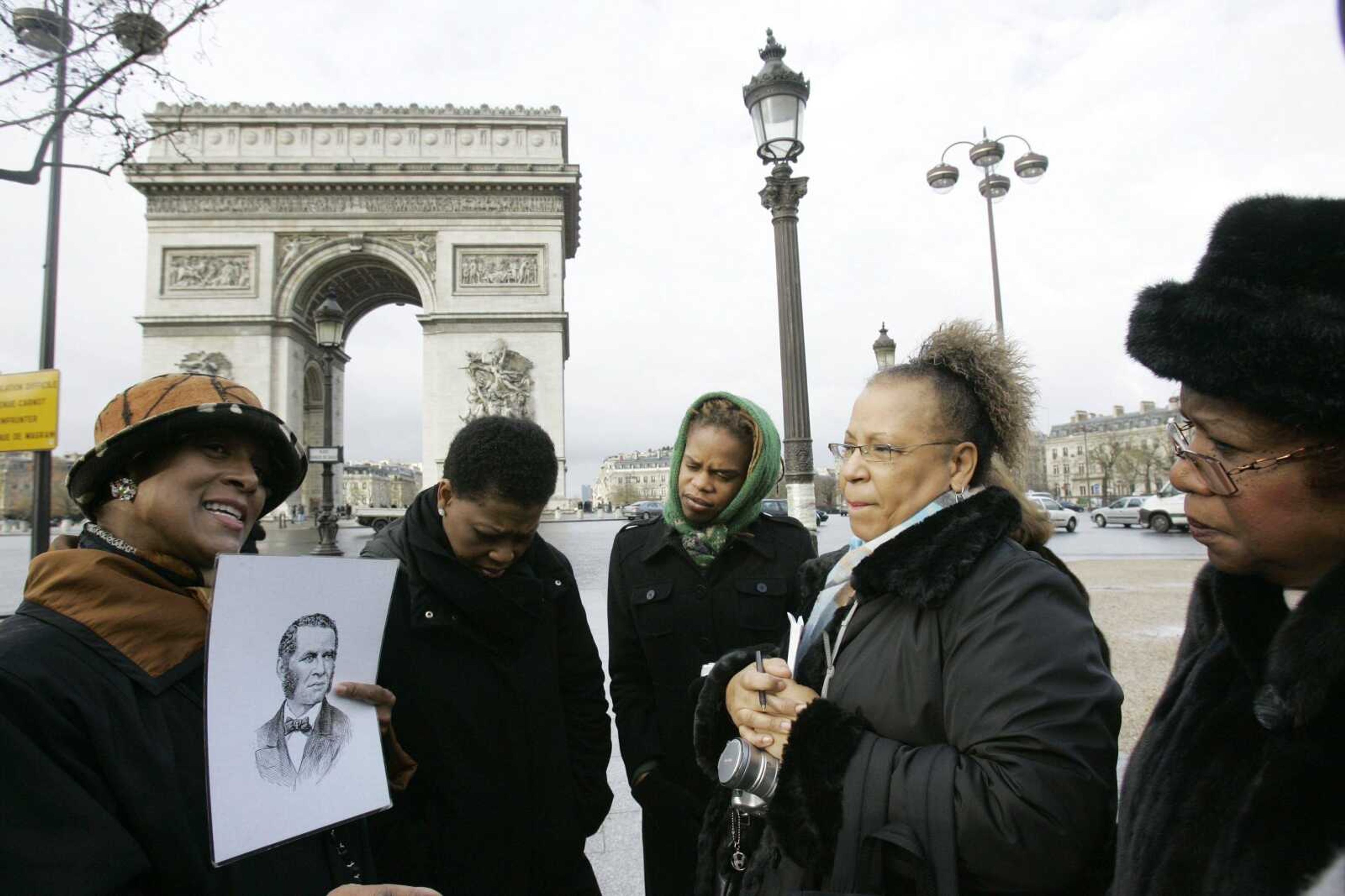 Tour guide Ricki Stevenson, left, an Oklahoma native, held a portrait of William Wells Brown, a 19th-century former slave turned abolitionist, while speaking to visitors near the Arc de Triomphe in Paris recently. Black Paris Tours offers a glimpse of the mutual love affair between African-Americans and the City of Light, and Africans' history in France as a whole. From right were Dora Morris, 59, retired elementary school teacher; Greta Burton, 52, realtor; Angela Morris, 28, a public health worker; all from Dallas, the other woman was unidentified. (CHRISTOPHE ENA ~ Associated Press)