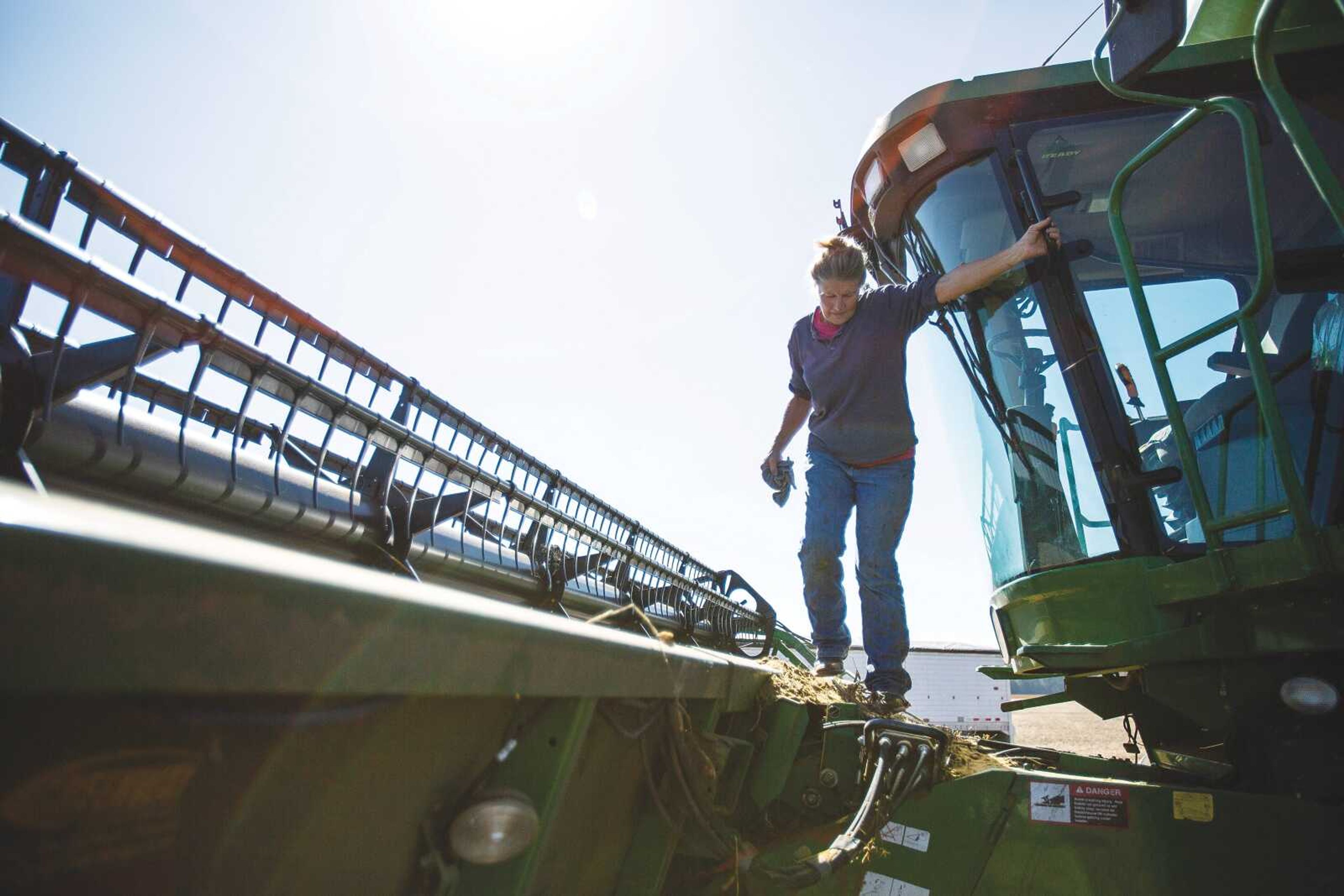 Susan Jahn climbs across the front of a combine, preparing it for a day of harvesting soybeans in one of many fields cultivated by Jahn Farms.
