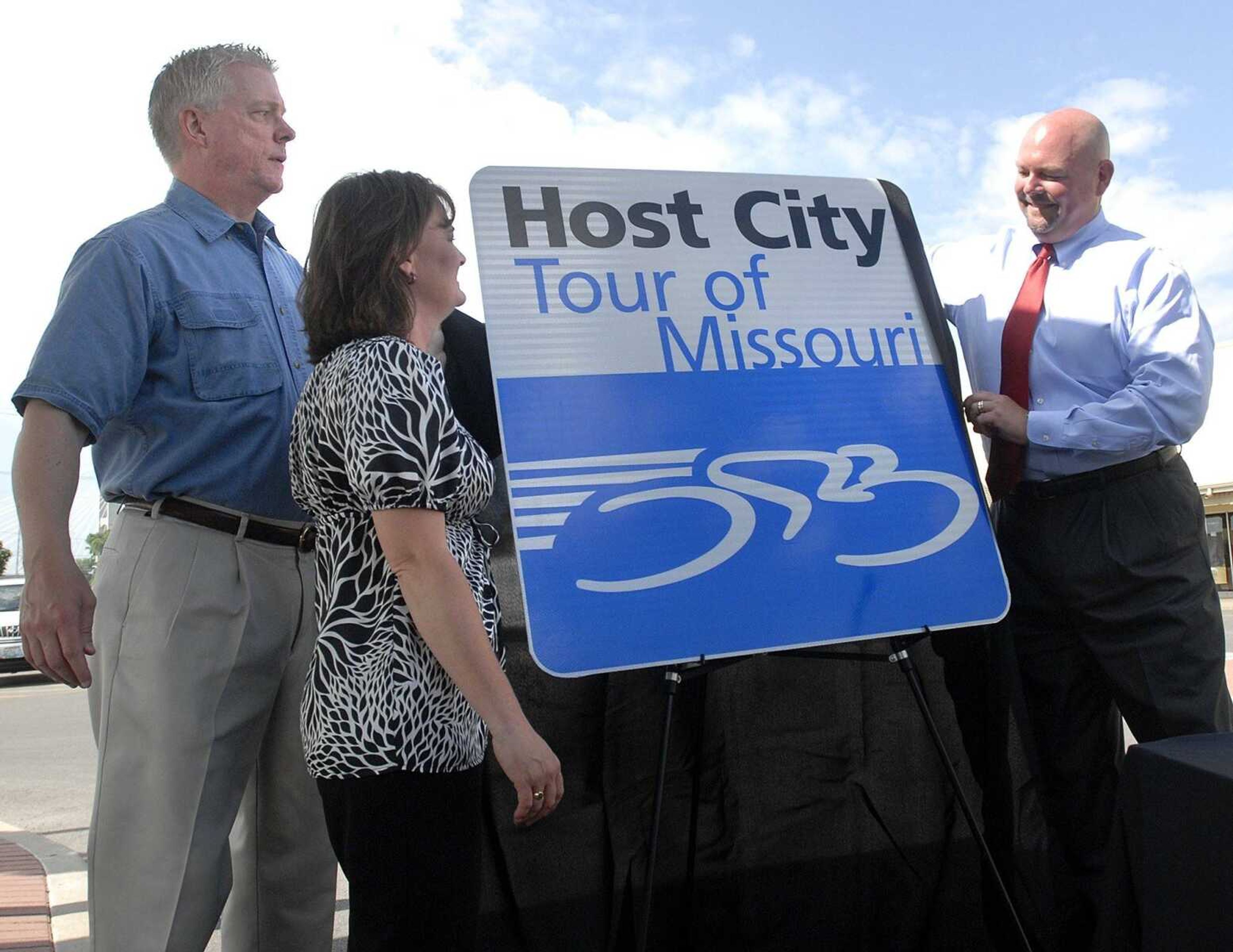 Lt. Gov. Peter Kinder, left, Tracey Glenn with the Cape Girardeau Area Chamber of Commerce, and Mayor Jay Knudtson unveil a "host city" sign for the Tour of Missouri bicycle race that will stop in Cape Girardeau Sept. 8. (Fred Lynch)