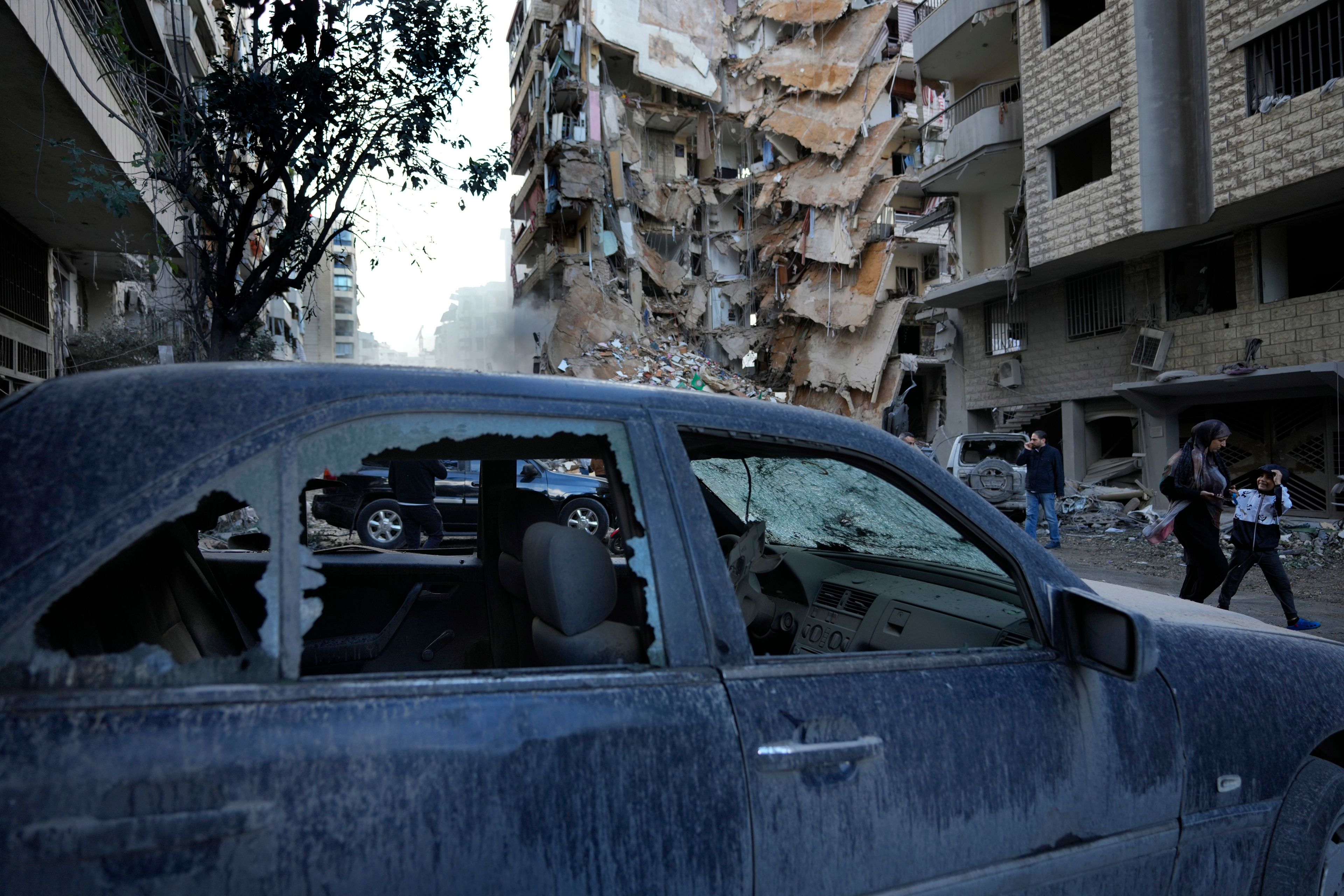 Residents pass in front of a destroyed building that was hit Sunday night in an Israeli airstrike in Dahiyeh, in the southern suburb of Beirut, Lebanon, Monday, Nov. 25, 2024. (AP Photo/Hussein Malla)