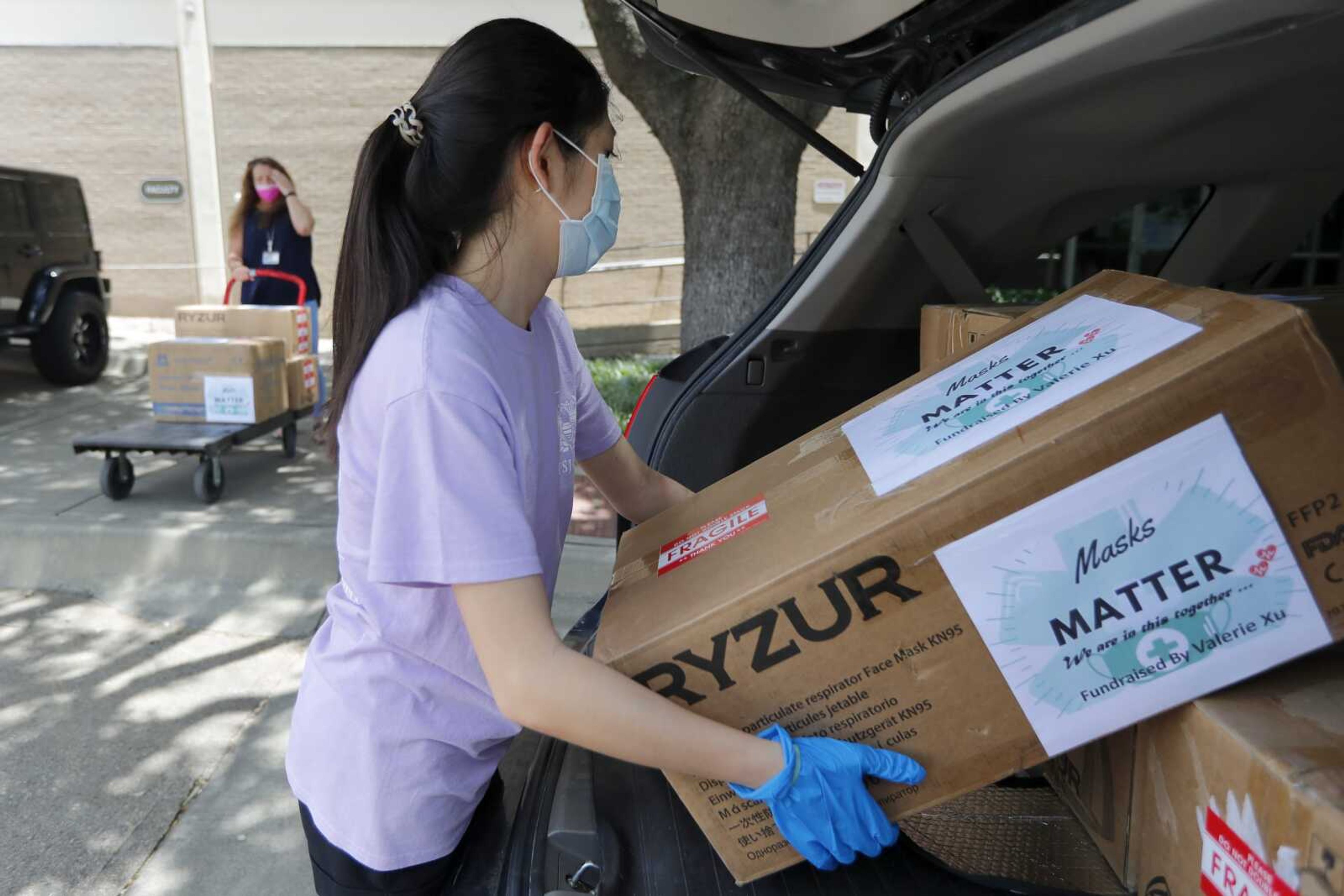 Valerie Xu, 15, carries boxes of masks June 5 to a waiting cart held by UT Southwestern Medical Center employee Cindy Levy  in Dallas. Xu raised the funds to buy the masks and make the donation to the hospital.