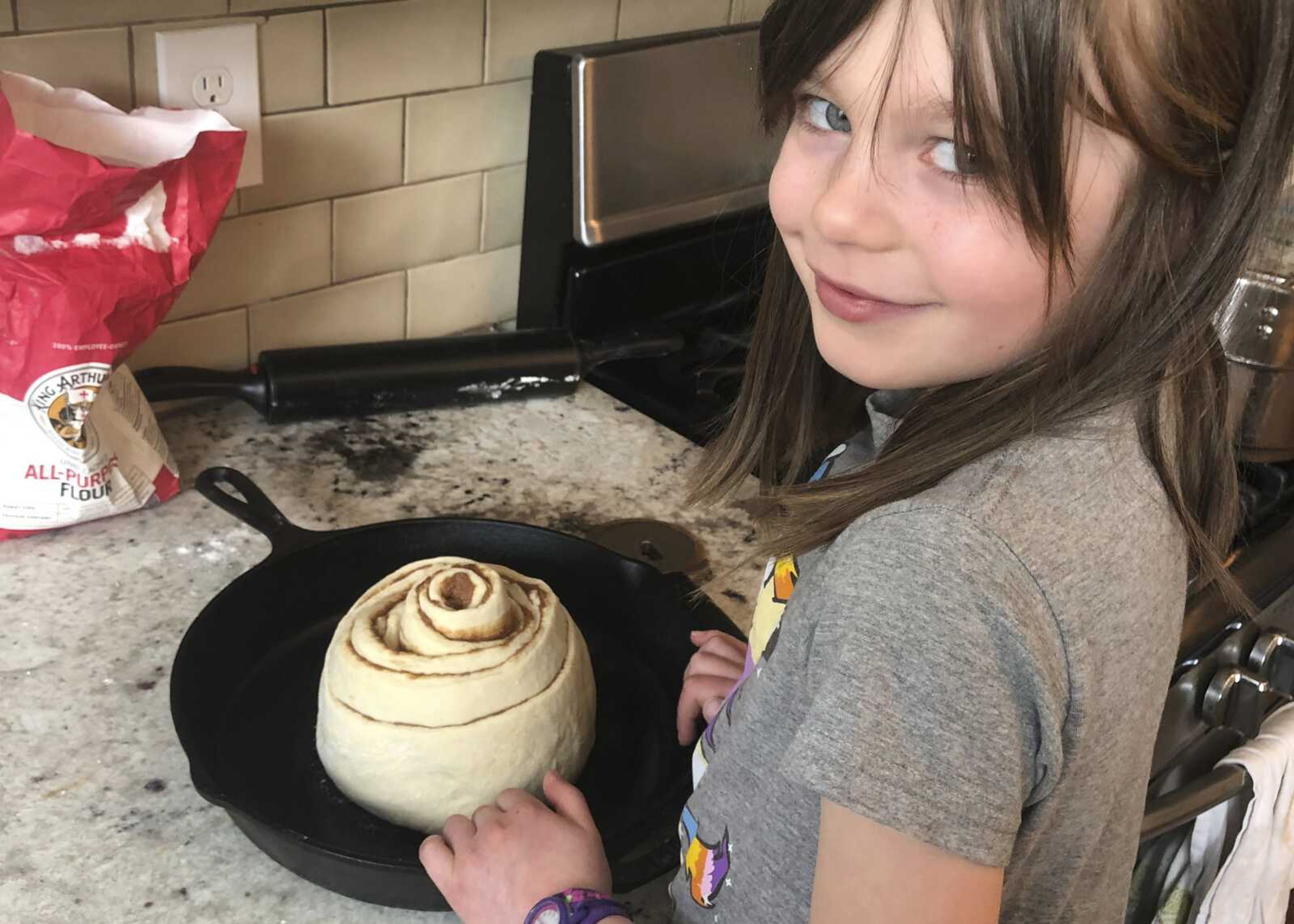 In this April 5 photo provided by Whitney Rutz, Elsa Rutz poses by a cinnamon roll at home in Portland, Oregon. Elsa's mother, Whitney, made cinnamon rolls to help raise funds for Oregon Food Bank.