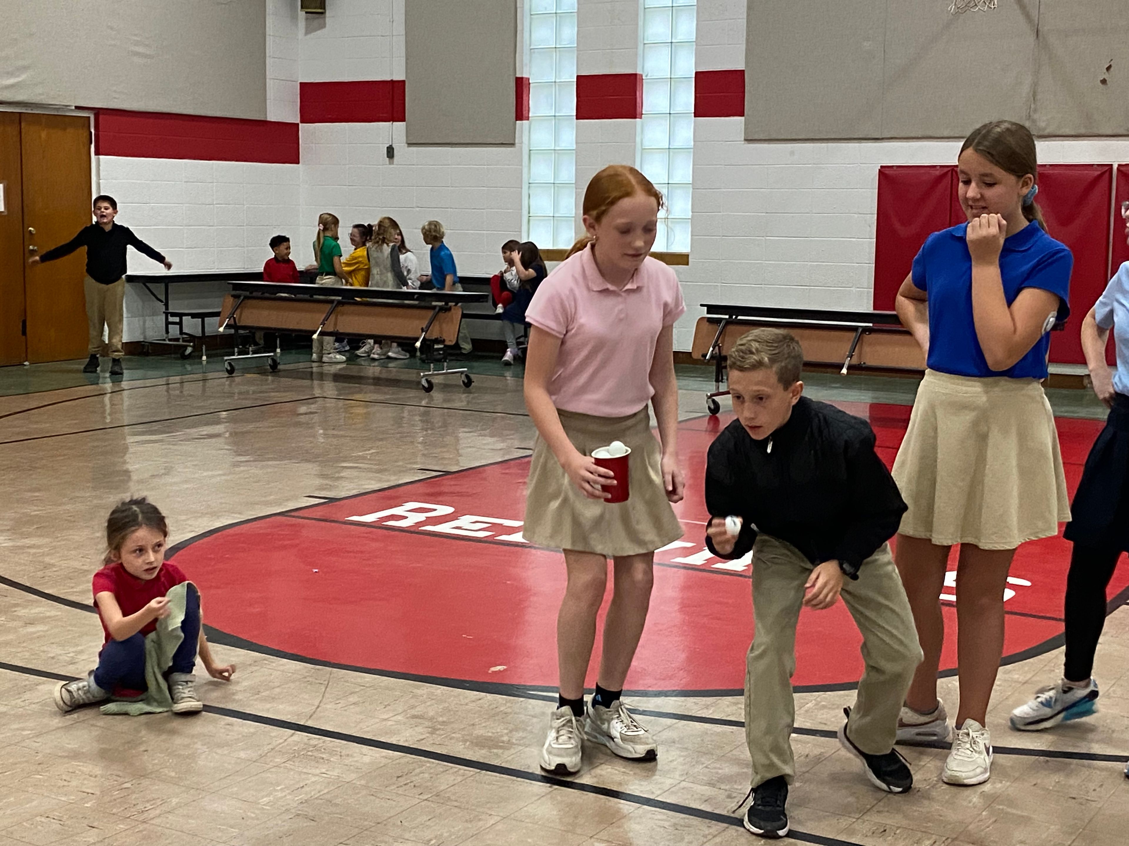 Tucker Hahn of St. Raphael's house gets in position to bounce a ping pong ball onto a peanut butter covered bread.  Mae Roper, Ashtyn Pobst, and Harper Gadberry watch on.
