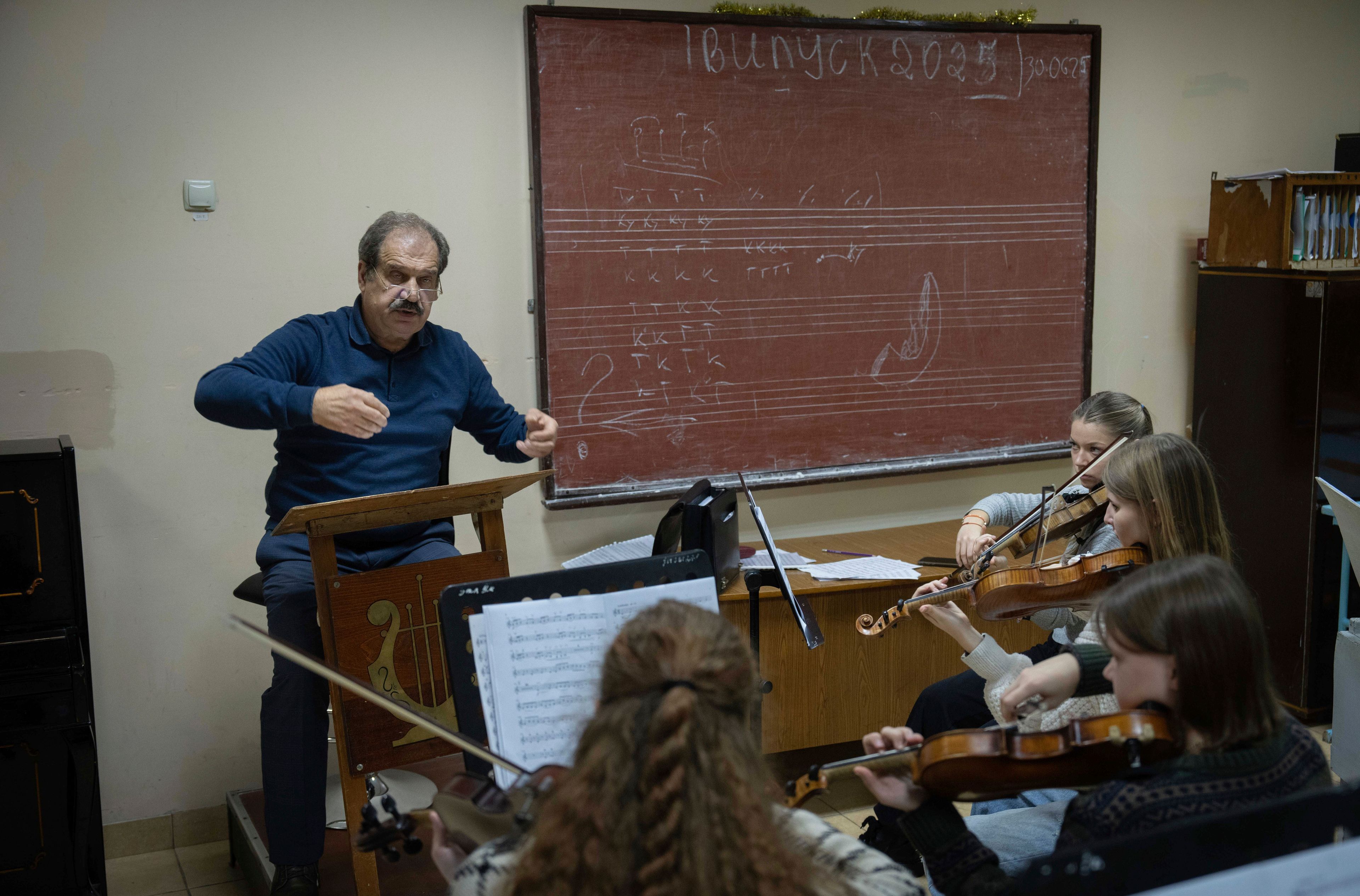 Volodymyr Sukhovetsky, a head of a music college, conducts a children's orchestra in a lesson in the basement shelter of his school during a Russian missile attack alert in Chernihiv, Ukraine, Monday, Nov. 11, 2024. (AP Photo/Efrem Lukatsky)