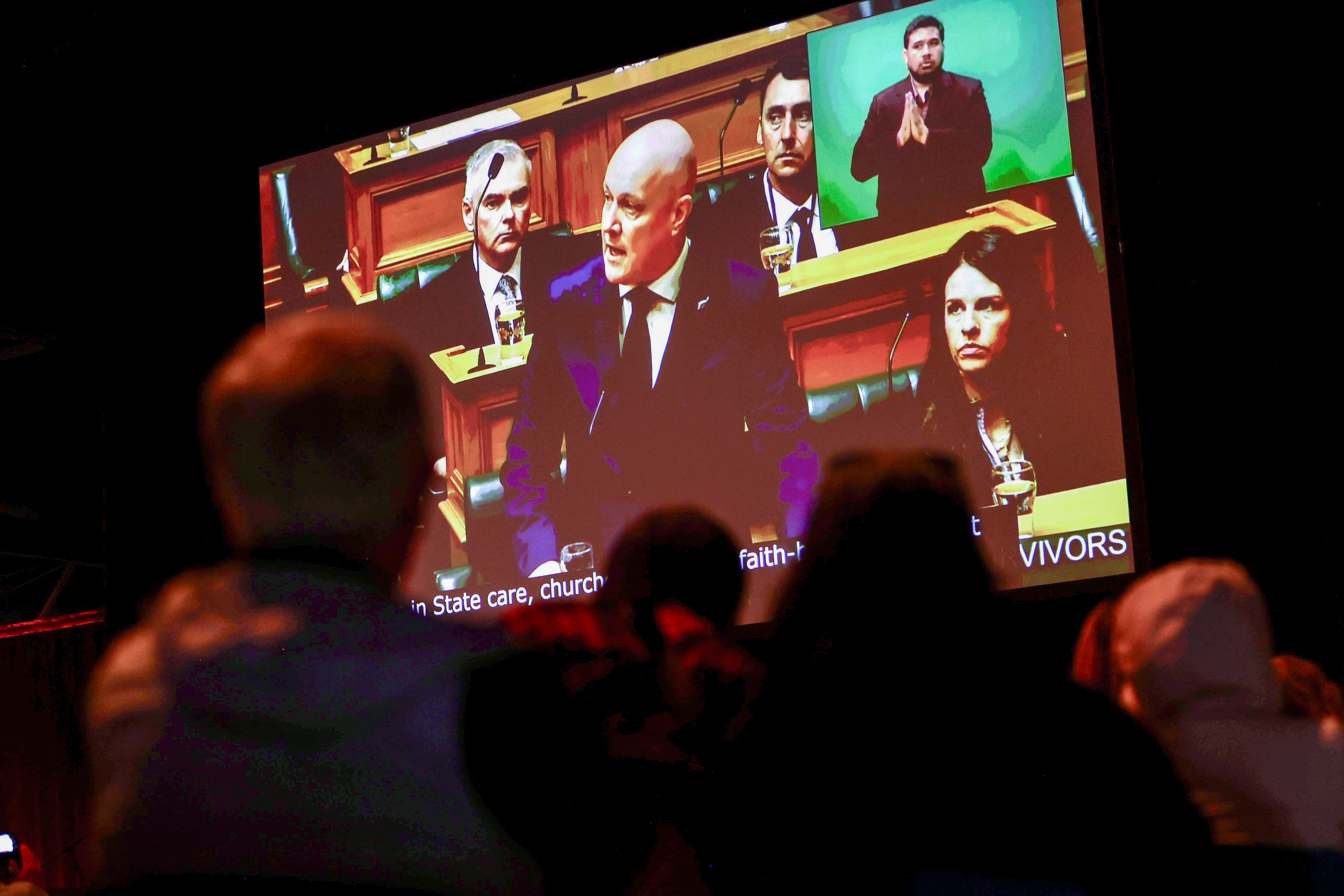 New Zealand's Prime Minister Christopher Luxon is shown on a screen as he makes a "formal and unreserved" apology in Parliament for the widespread abuse, torture and neglect of hundreds of thousands of children and vulnerable adults in care, in Wellington, New Zealand, Tuesday, Nov. 12, 2024. (Lawrence Smith/Stuff via AP )