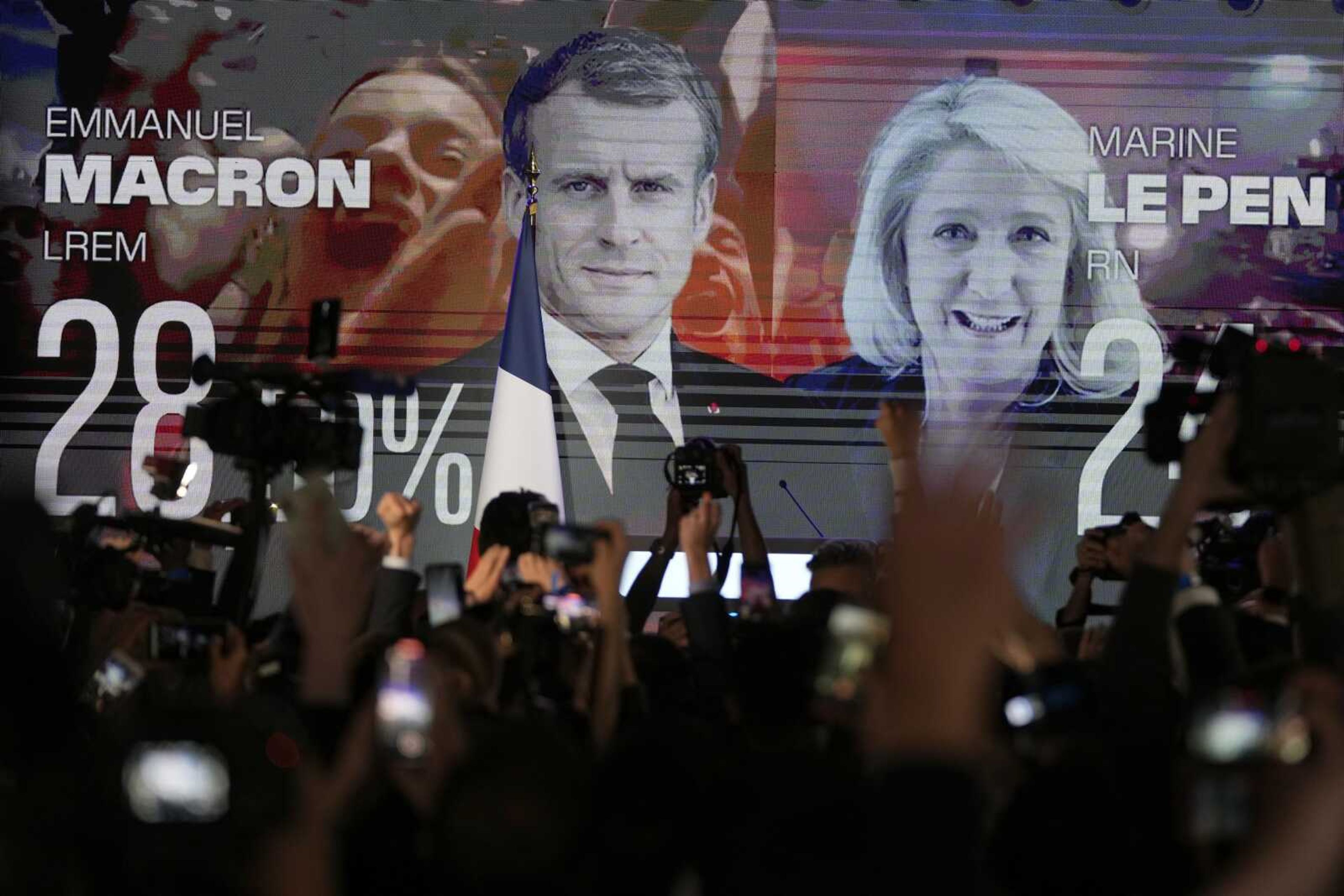 A screen shows French President Emmanuel Macron, centrist candidate for reelection, and far-right candidate Marine Le Pen at her election day headquarters Sunday in Paris. French polling agency projections show incumbent Macron and Le Pen leading in the first round of France's presidential election Sunday.