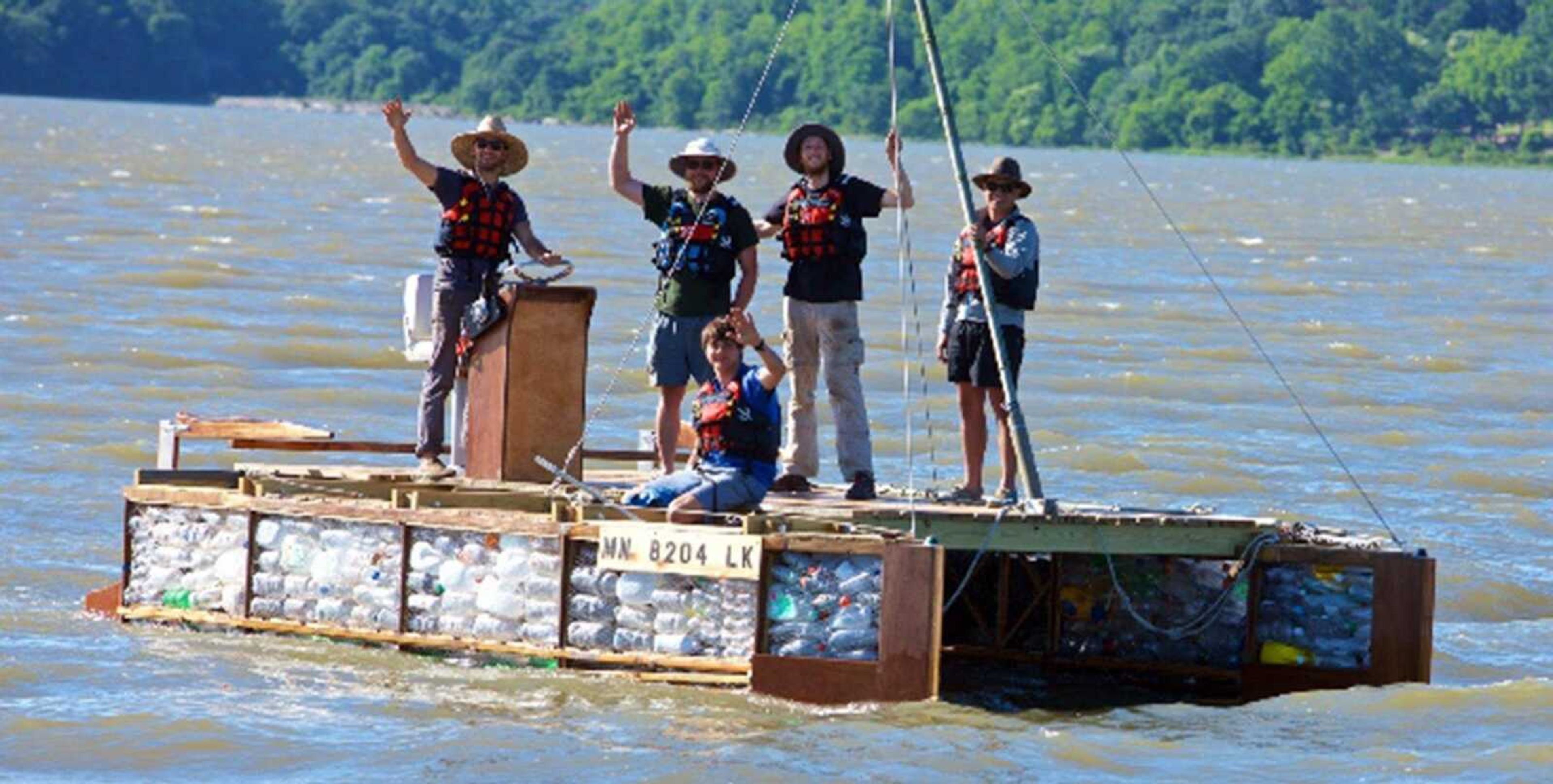 The crew of the Recycled Mississippi expedition wave from their craft made of repurposed wood and plastic bottles.