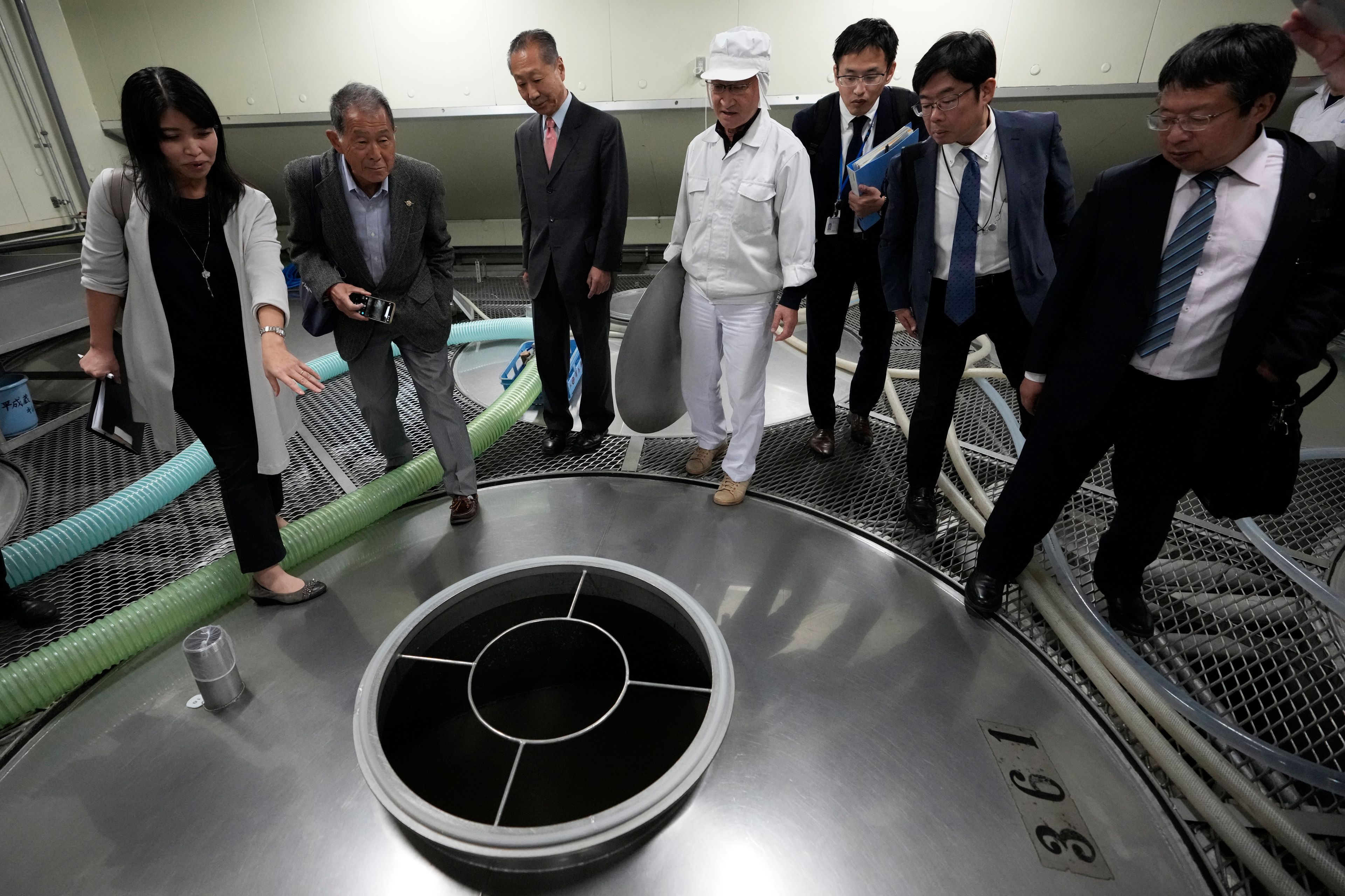 An interpreter, left, translates for Junichiro Ozawa, head of Ozawa Sake Brewery, third left, and his worker (in white) as Hitoshi Utsunomiya, far right, director of the Japan Sake and Shochu Makers Association, stands during a media tour at the brewery in Ome, on the western outskirts of Tokyo, Japan, Wednesday, Nov. 13, 2024. (AP Photo/Hiro Komae)