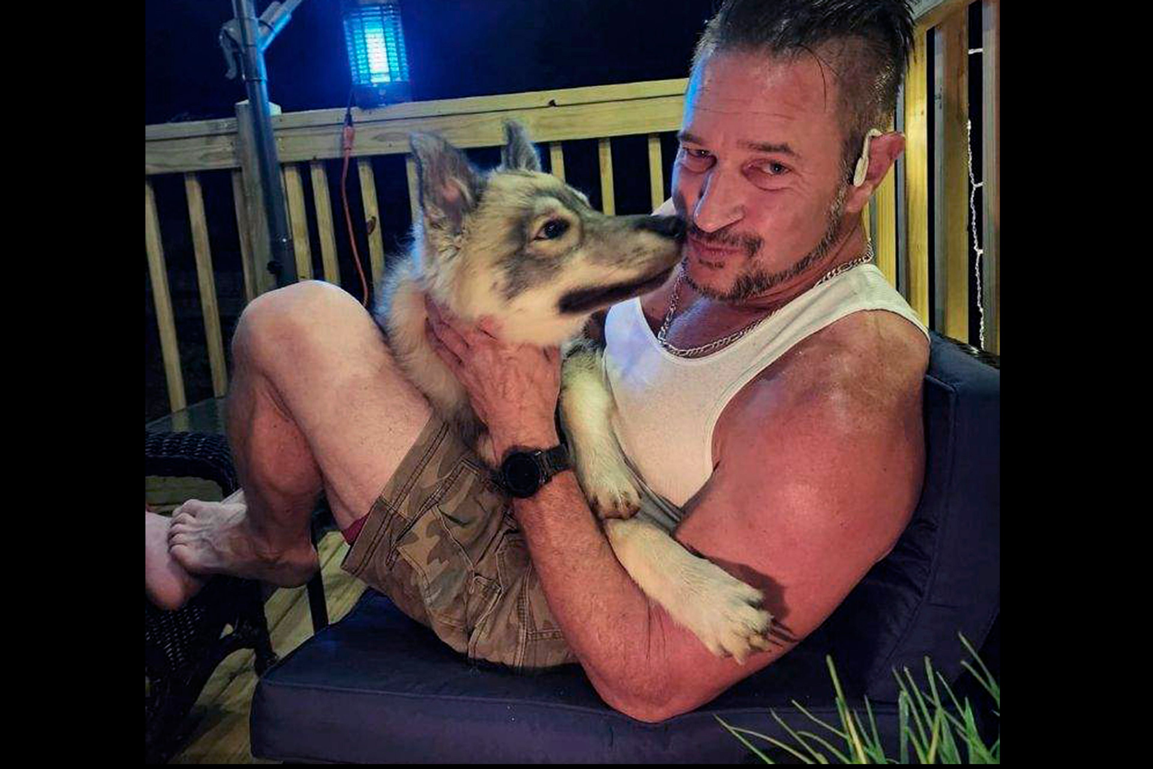 This image provided by pet owner Kirk Rumford, pictured, shows him getting licked by his dog Odin, a husky, which was accidentally shot and killed by an animal control officer on Tuesday Nov. 19, 2024, in Northbridge, Mass. Odin was mistaken for a coyote in an incident that local police are describing as a sad mix-up. (Kirk Rumford via AP)