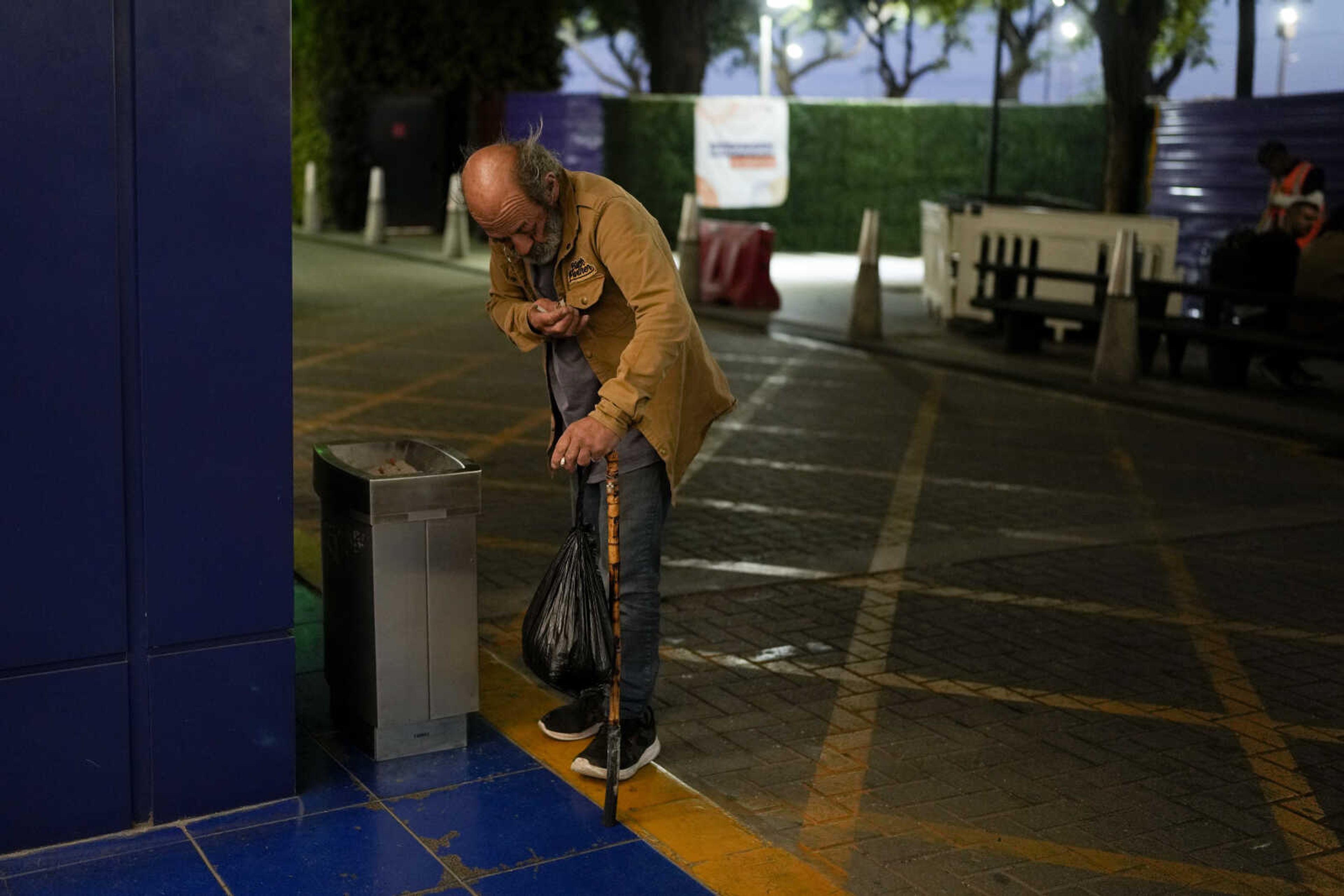 Angel Gomez looks for discarded cigarettes in an ashtray outside at the Jorge Newbery international airport, commonly known as Aeroparque, in Buenos Aires, Argentina, Thursday, April 6, 2023. Gomez, who sleeps at Aeroparque each evening, says that the airport is a good option for sleeping because there is air conditioning in the summer and heating in the winter. (AP Photo/Natacha Pisarenko)