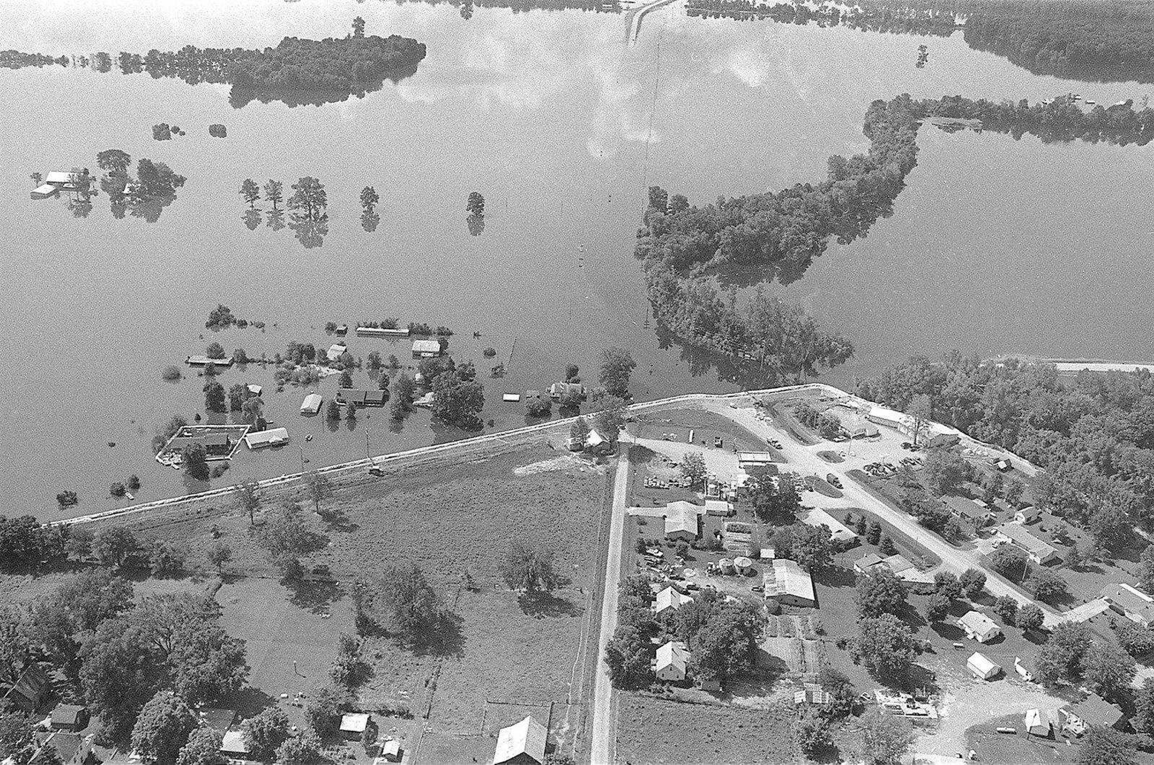 A temporary sandbag levee along Highway 74 at Dutchtown protects the town from floodwaters of the Diversion Channel during the 1993 Mississippi River flood that crested at 48.49 feet Aug. 8 at Cape Girardeau. This view looking south over Dutchtown shows Highway 25 in the center covered with water and continuing north through the town, shown in the right corner foreground.