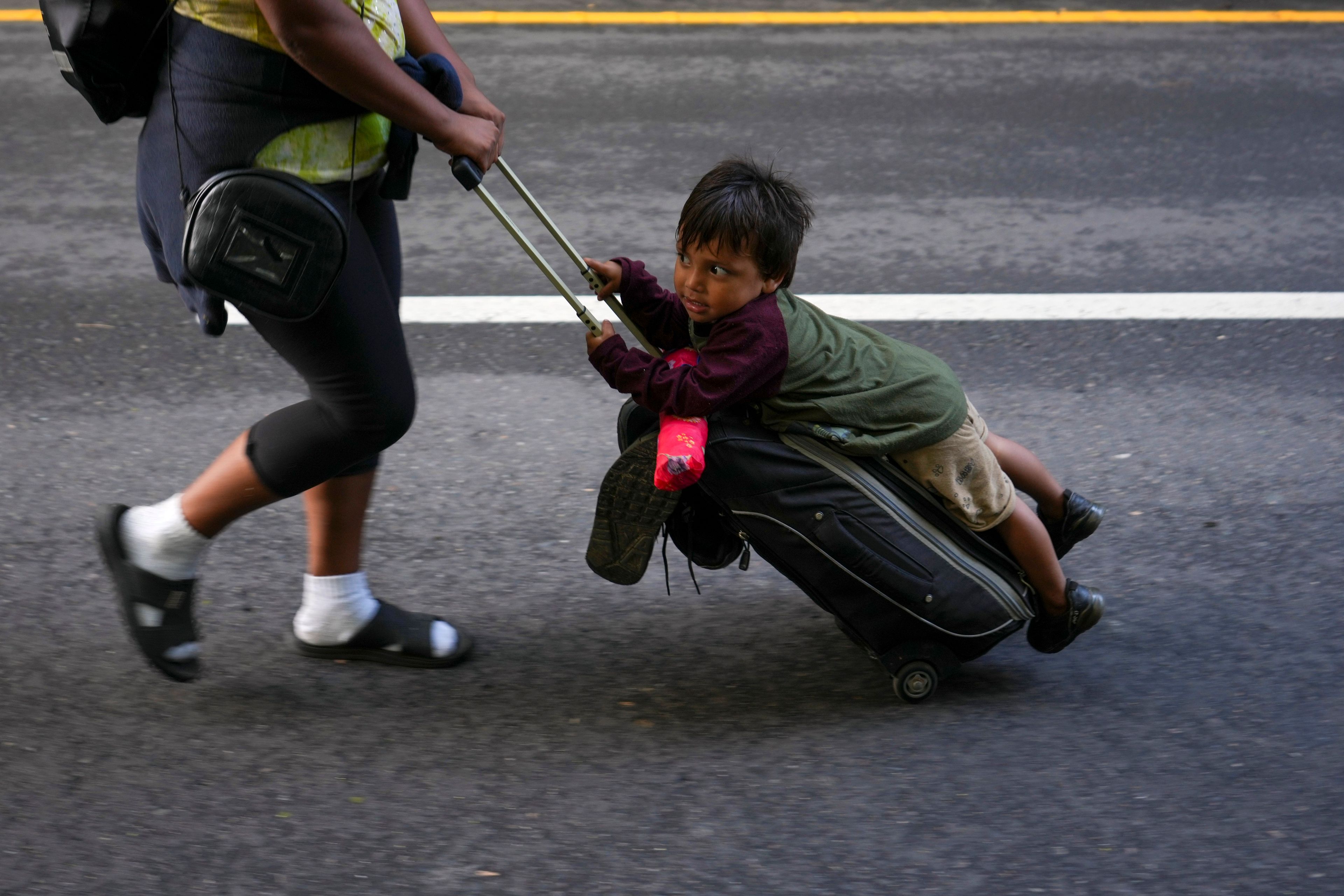 Nayely Nunez, from Honduras, uses her luggage to carry a child as she walks along the highway with a migrant caravan in Huixtla, southern Mexico, heading toward the country's northern border and ultimately the United States, Thursday, Nov. 7, 2024. (AP Photo/Moises Castillo)