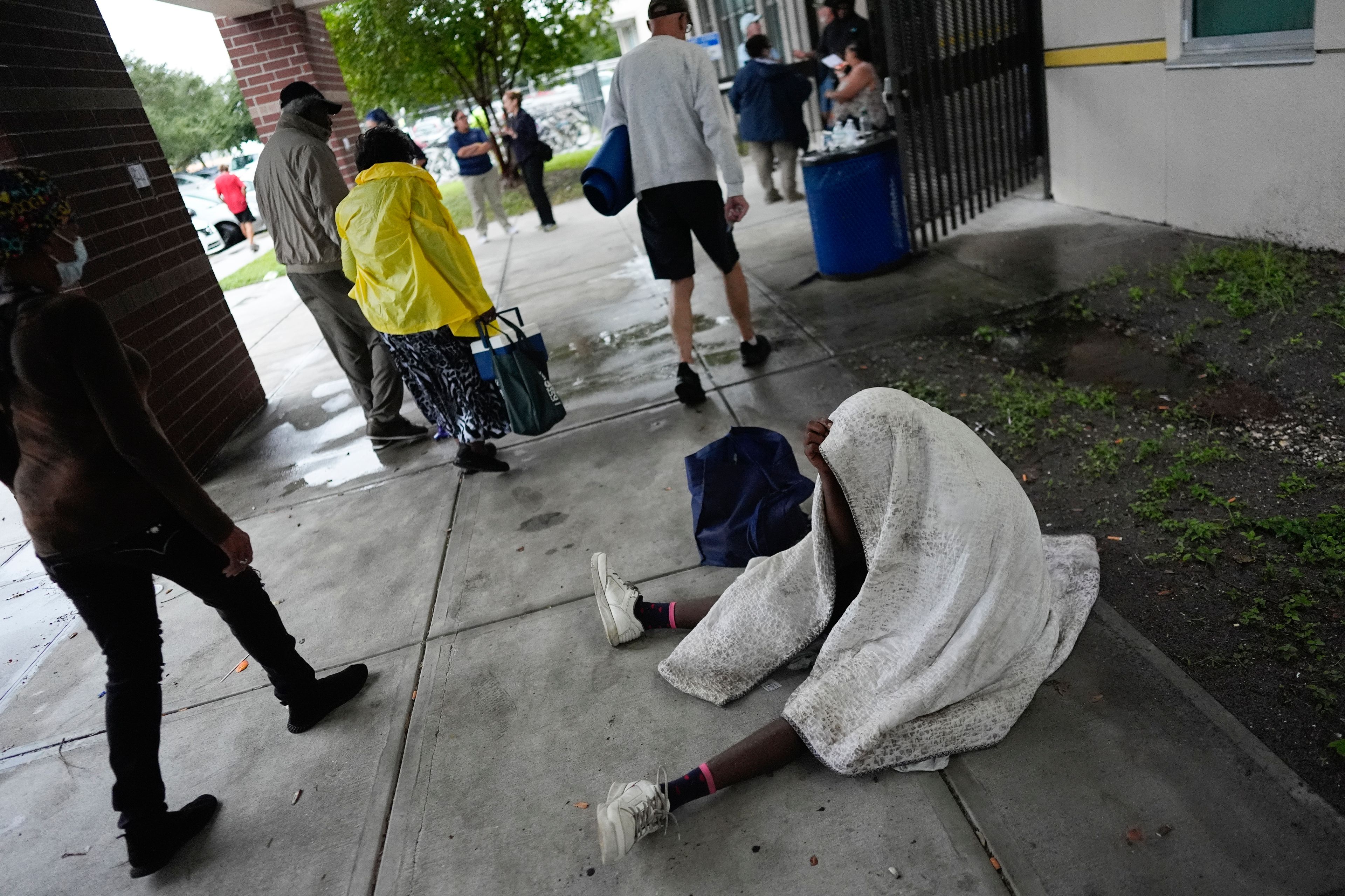 A man rests as other carry supplies into Gibbs High School, a government storm shelter where 1,700 people had already sought shelter by late morning, ahead of the arrival Hurricane Milton, in St. Petersburg, Fla., Wednesday, Oct. 9, 2024. (AP Photo/Rebecca Blackwell)