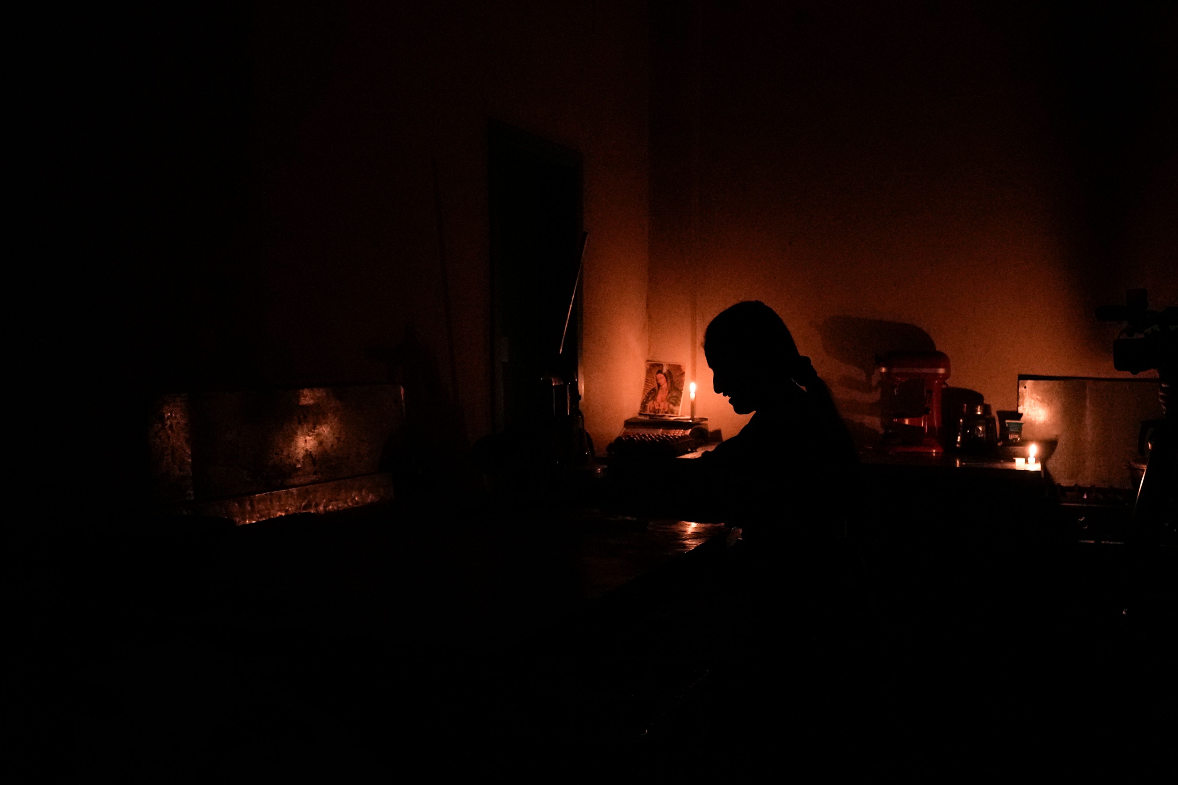 Monica Valiente waits for customers in her candle-lit bakery during a rolling blackout in Quito, Ecuador, Oct. 15, 2024. (AP Photo/Dolores Ochoa)