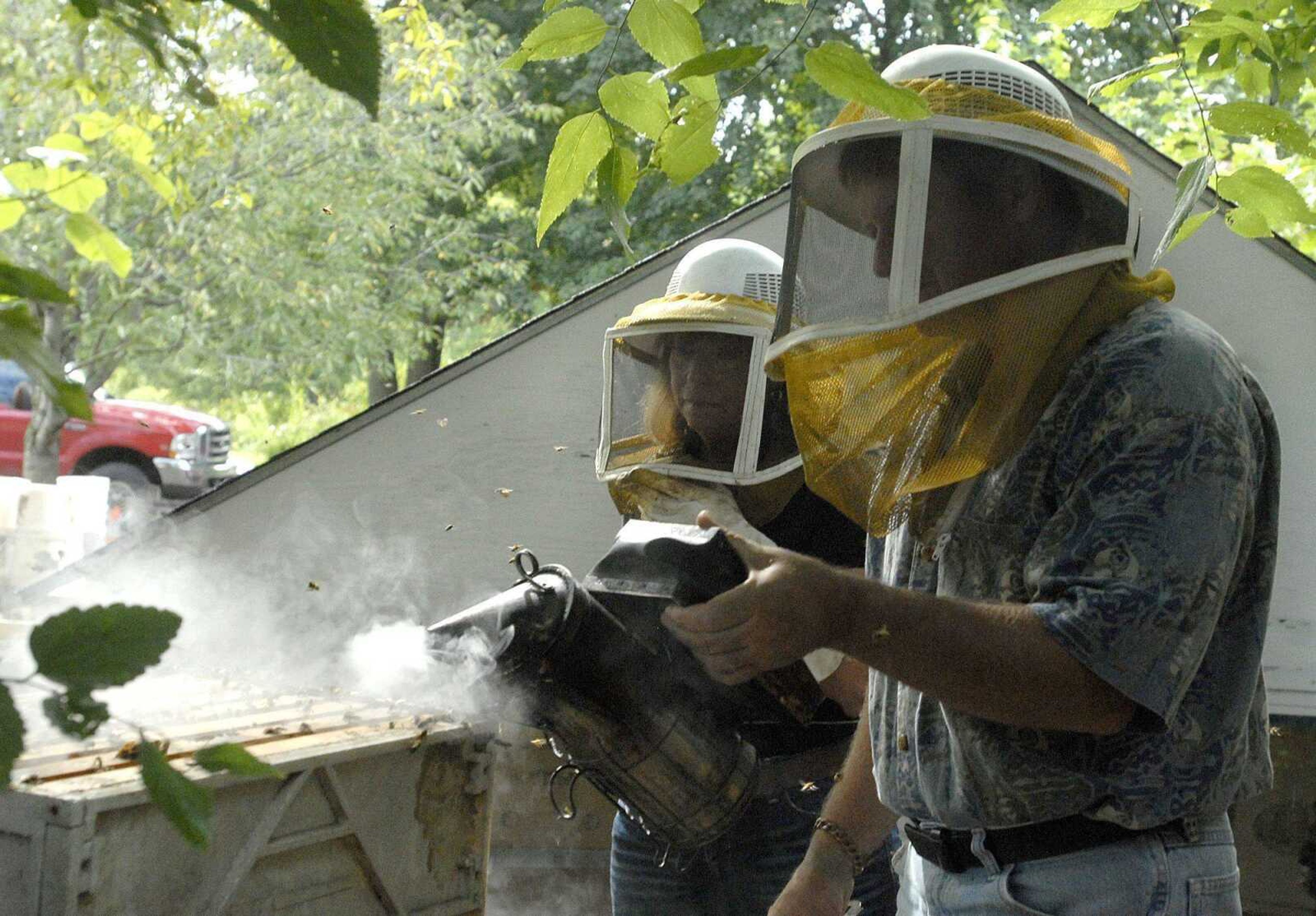 Grant Gillard uses a smoker to help calm honey bees in the hive body at his Jackson, Mo. bee farm Friday morning, Aug. 19, 2011 as U.S. Rep. Jo Ann Emerson observes as part of her annual Emerson Farm Tour. (Laura Simon)