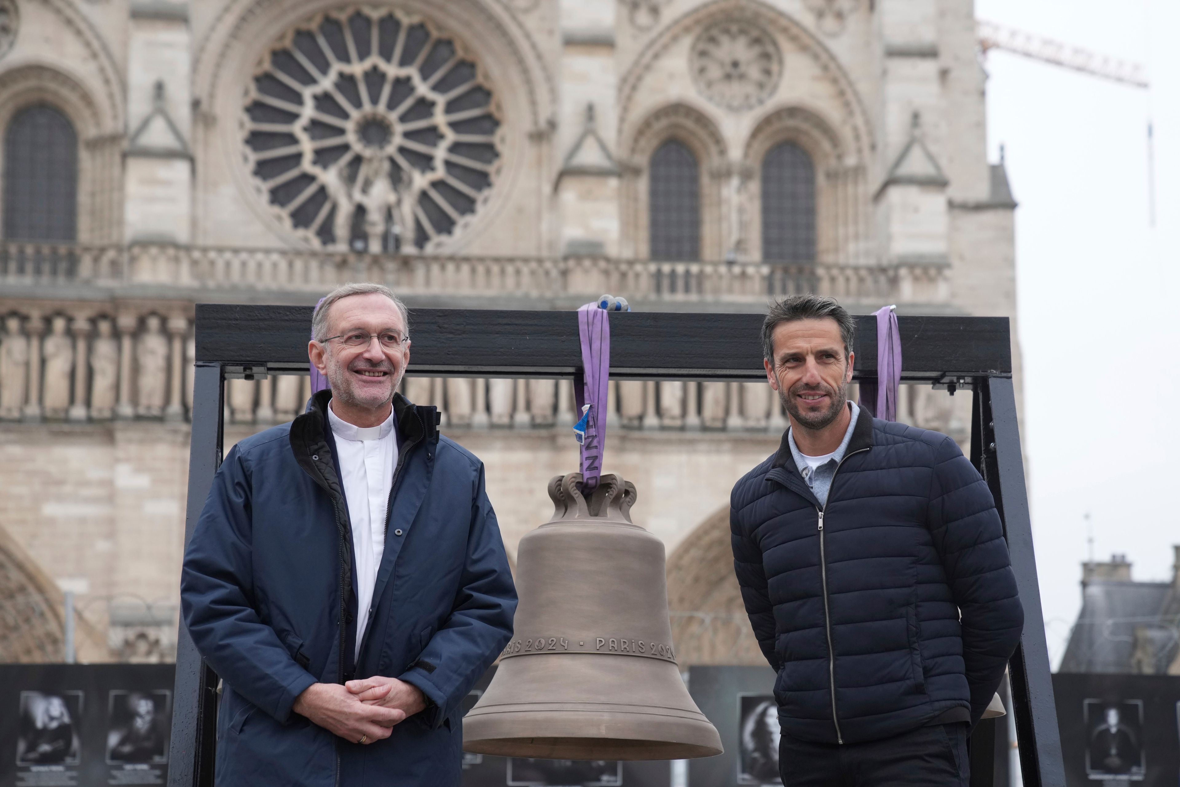 Tony Estanguet, right, head of Paris 2024 Olympic Games, and Notre-Dame cathedral rector Olivier Ribadeau Dumas pose next to the bell that Olympic medalists rang at the Paris Games, before its installation in Notre Dame Cathedral, ahead of the monument's grandiose reopening following a massive fire and five-year reconstruction effort, Thursday, Nov. 7, 2024 in Paris. (AP Photo/Christophe Ena)