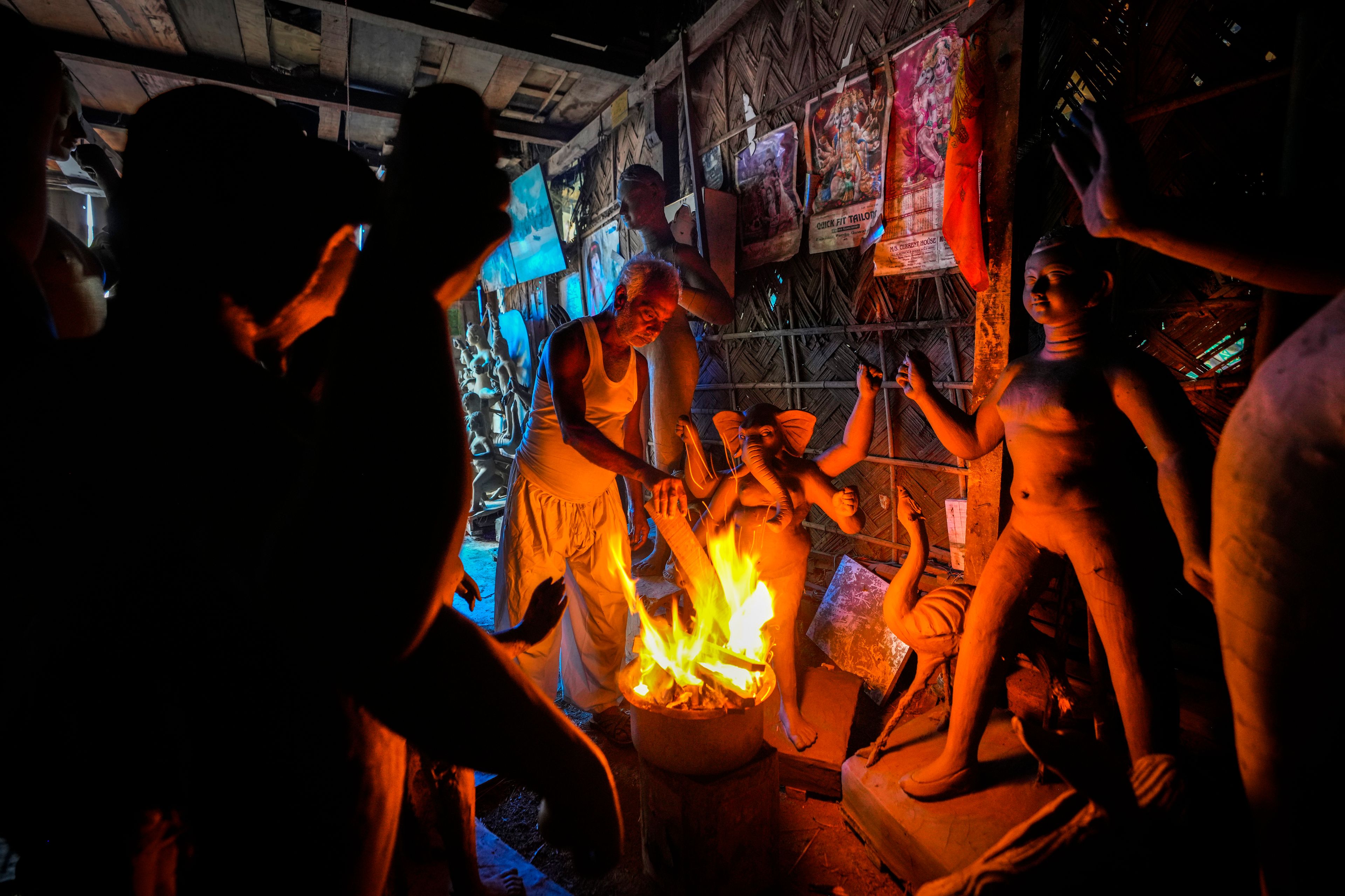 Ratan Paul, 70, lights a wood fire to dry mud idols of the Hindu gods and goddesses at his workshop during the Durga Puja festival in Guwahati, India, Friday, Oct. 4, 2024. (AP Photo/Anupam Nath)