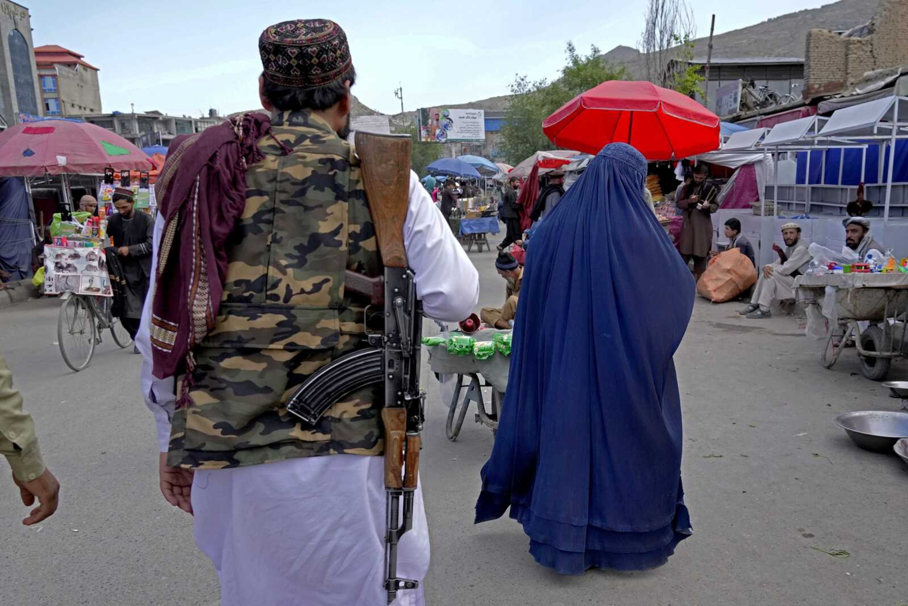 A woman wearing a burqa walks through the old market as a Taliban fighter stands guard Sunday in downtown Kabul, Afghanistan.