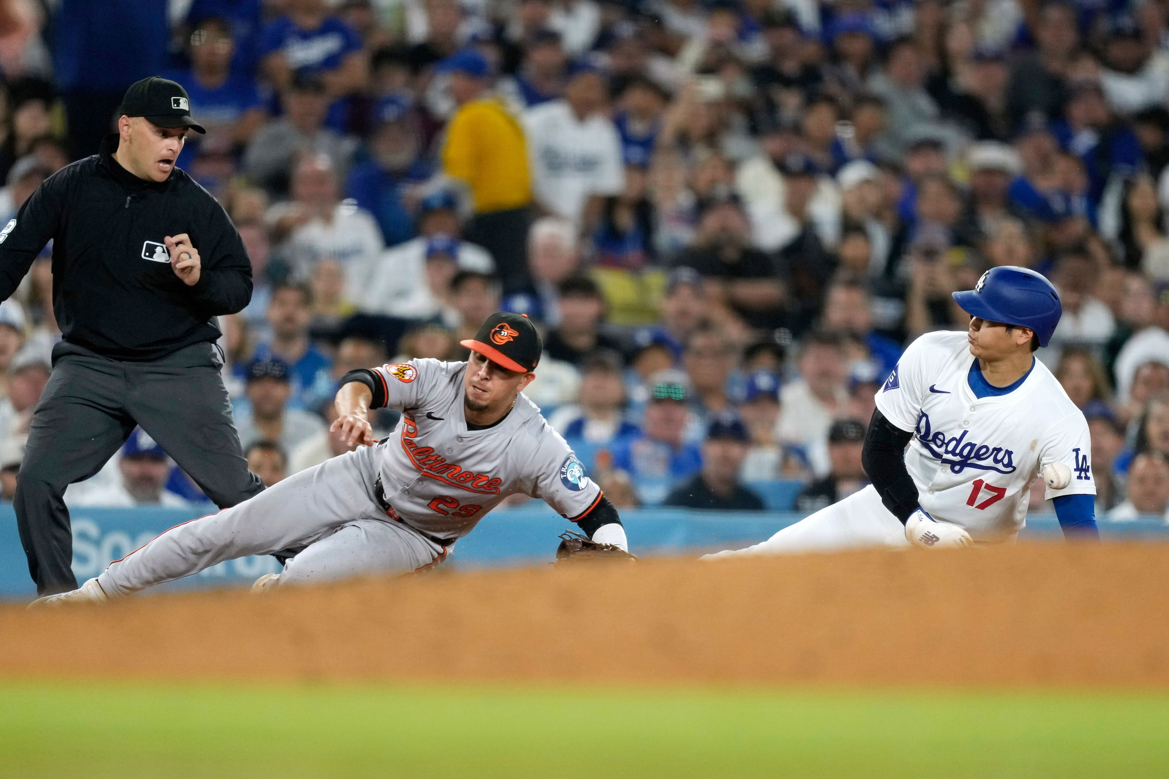 Los Angeles Dodgers' Shohei Ohtani, right, is hit by a ball thrown from home plate as he steals third while Baltimore Orioles third baseman Ramon Urias misses the ball and third base umpire Jansen Visconti watches during the third inning of a baseball game Wednesday, Aug. 28, 2024, in Los Angeles. (AP Photo/Mark J. Terrill)