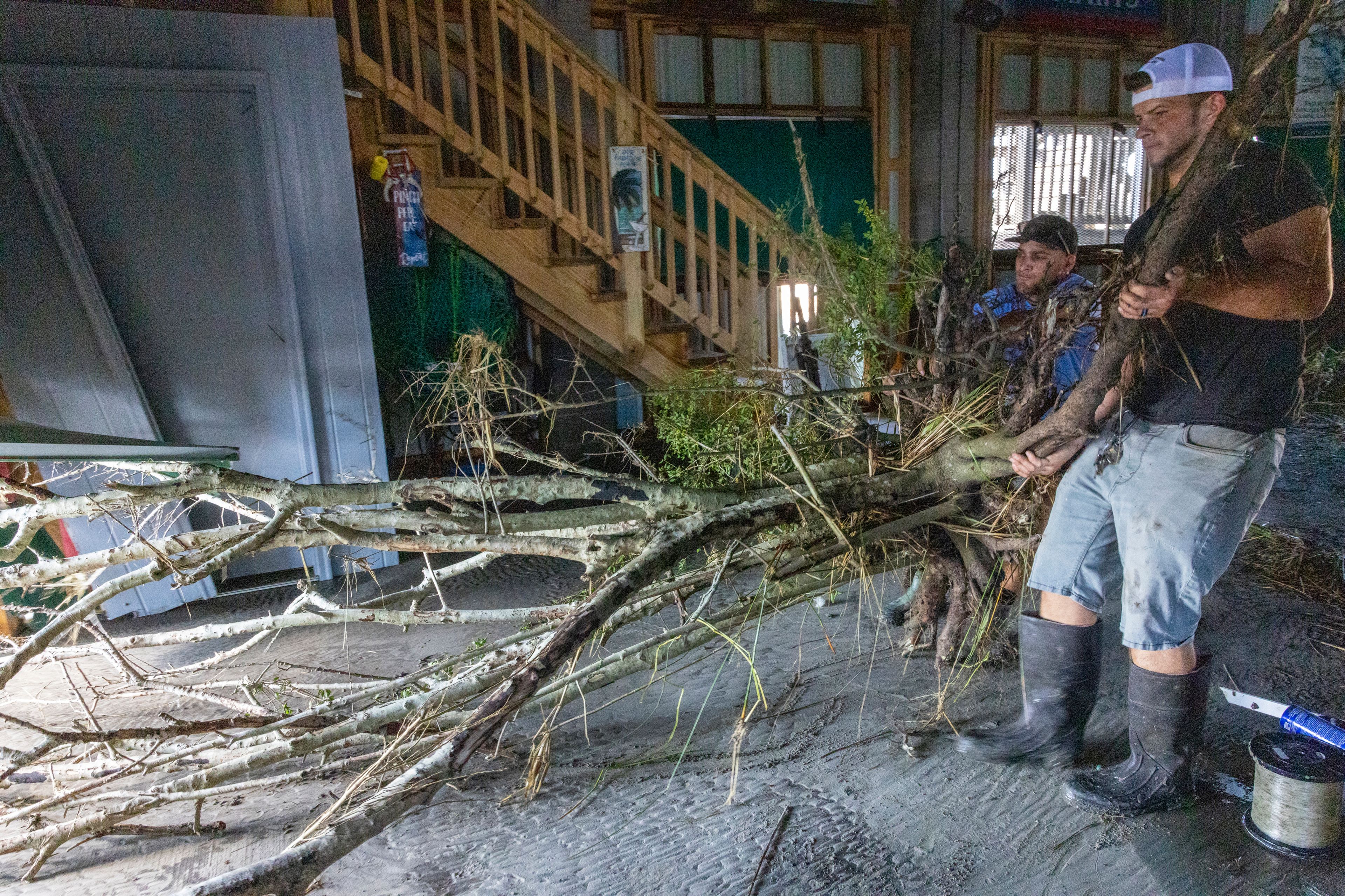 Jansen Pellegrin, back right, and Drew Foret, right, remove a small tree that floated into a living room area at their fishing camp from Hurricane Francine in Terrebonne Parish, La., Thursday, Sept. 12, 2024. (Chris Granger/The Times-Picayune/The New Orleans Advocate via AP)