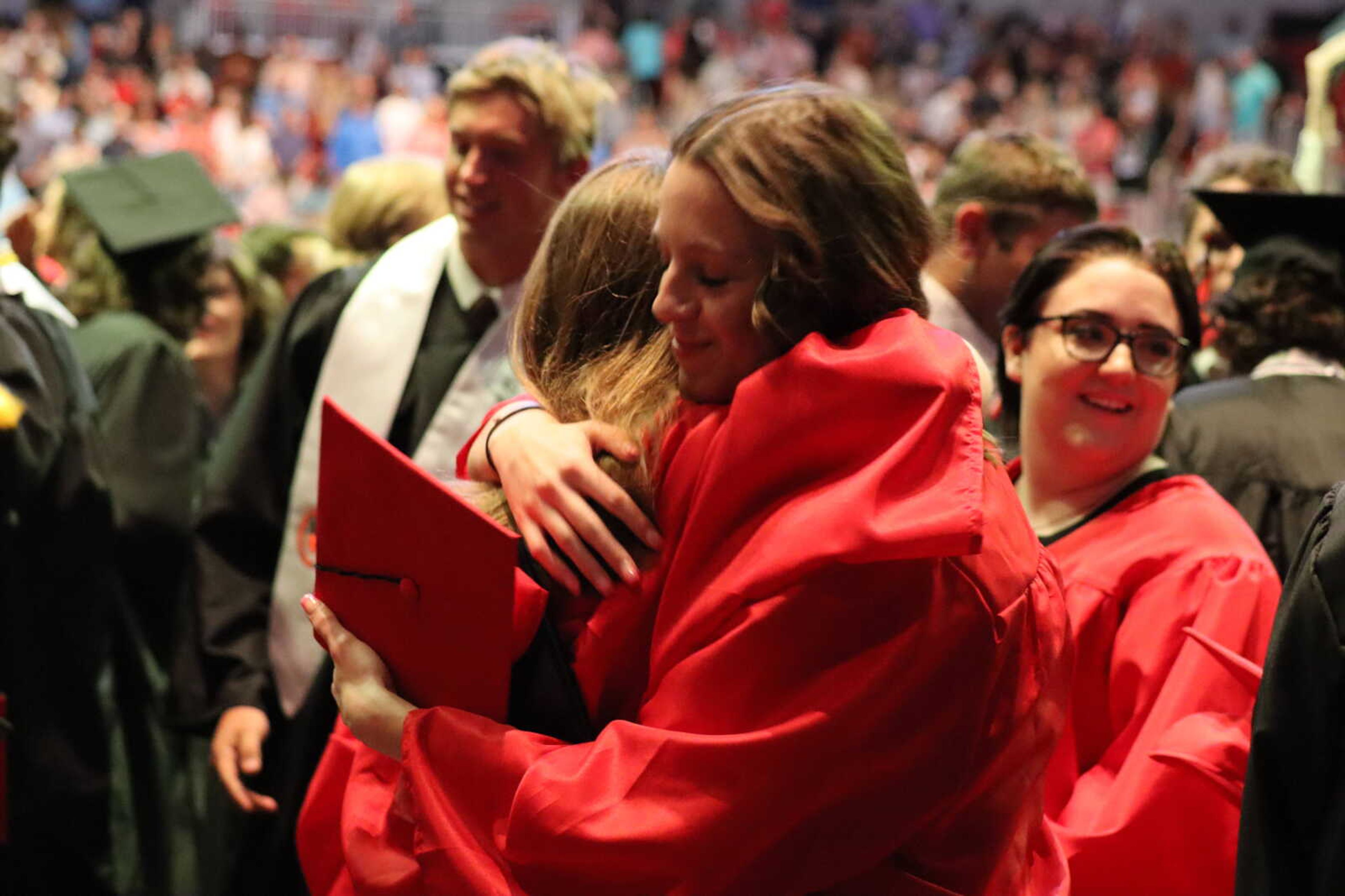 Two graduates hug in celebration after earning their diplomas.