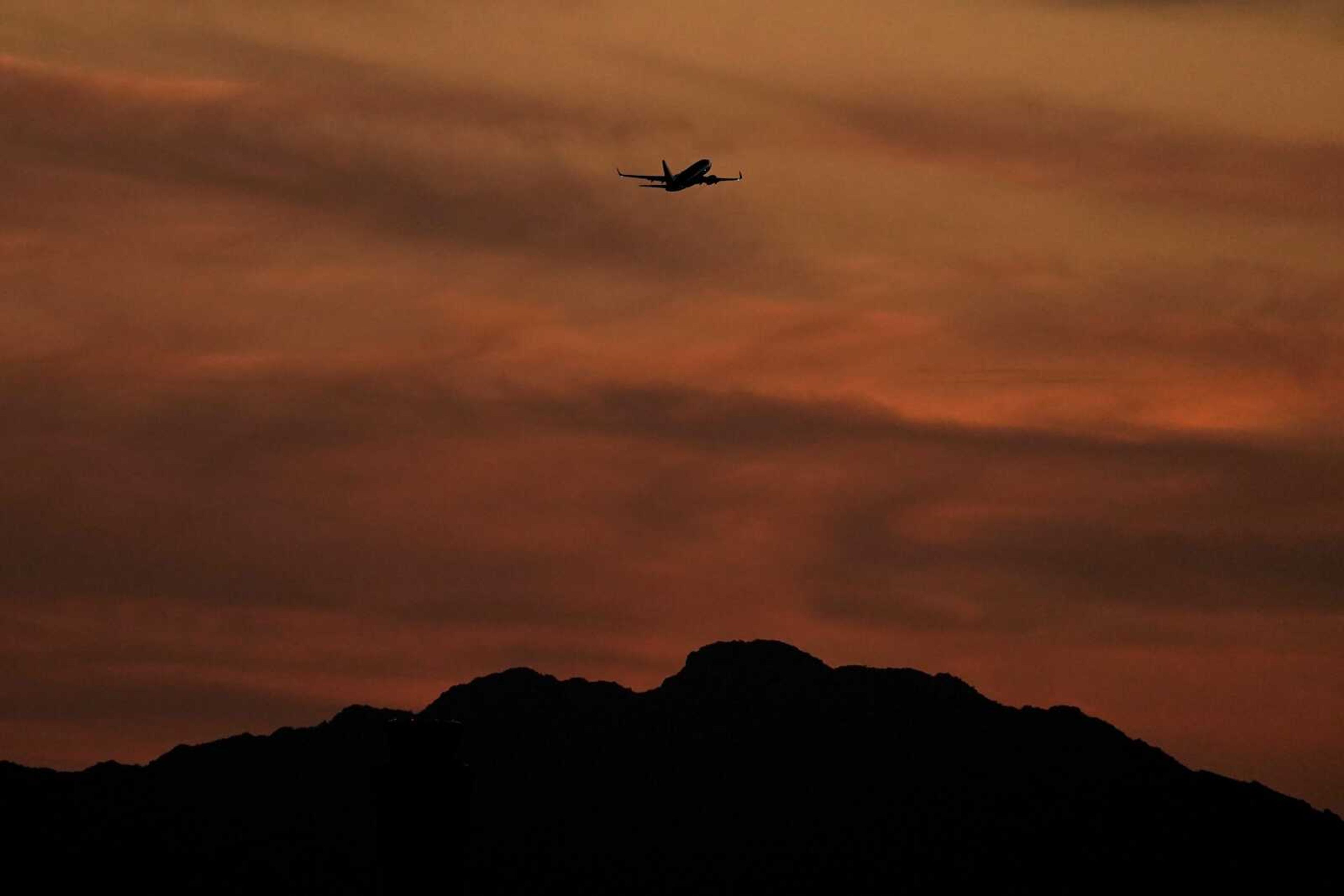 A passenger jet is silhouetted against the sky at dusk as it takes off from Sky Harbor Airport on Saturday in Phoenix. Airlines have canceled more than 3,500 U.S. flights over the weekend and delayed thousands more, citing weather in Florida and other issues.